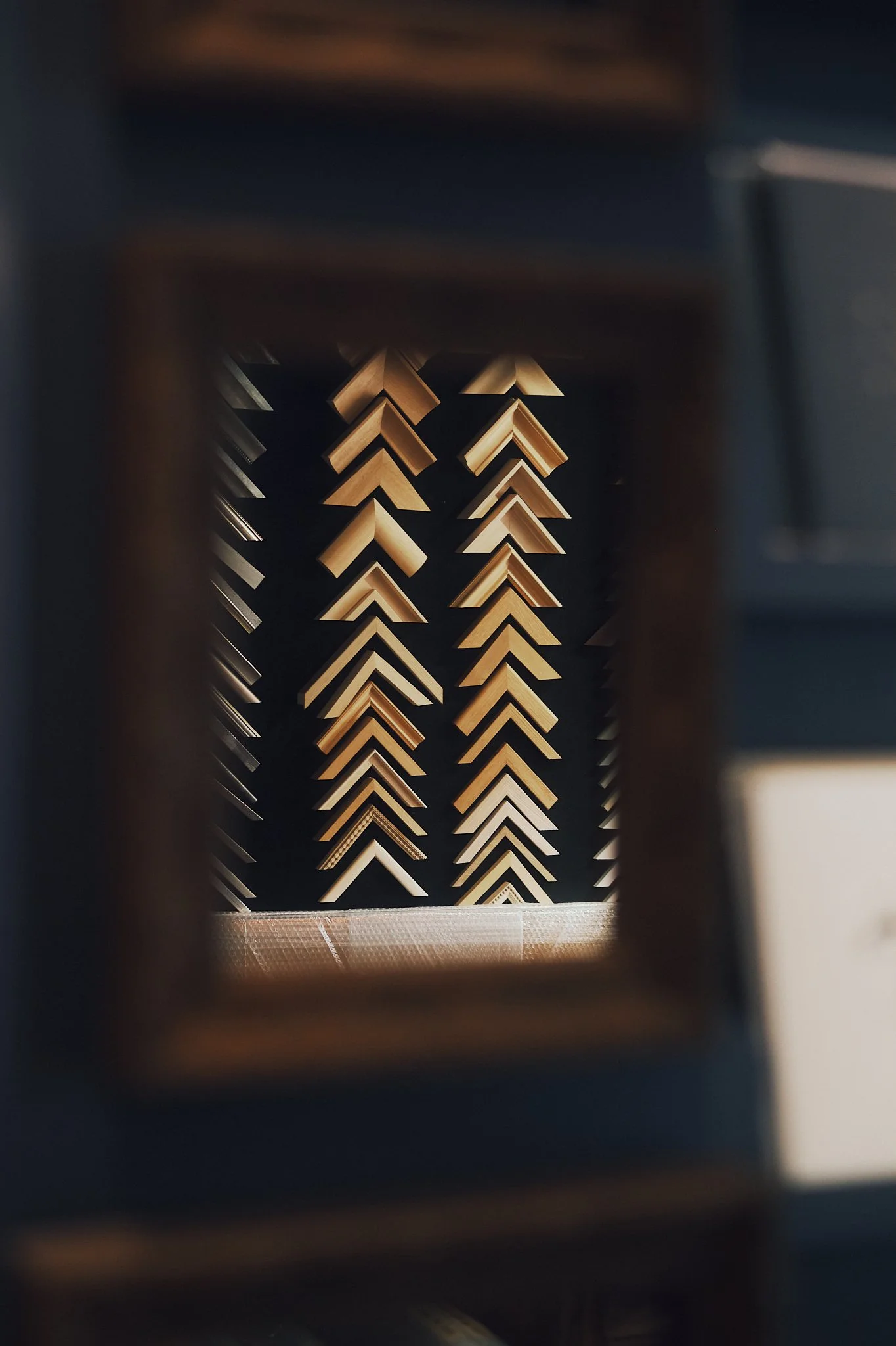 Close-up of wooden corner trim pieces arranged in a tall, narrow display within a frame, viewed through a blurred foreground.