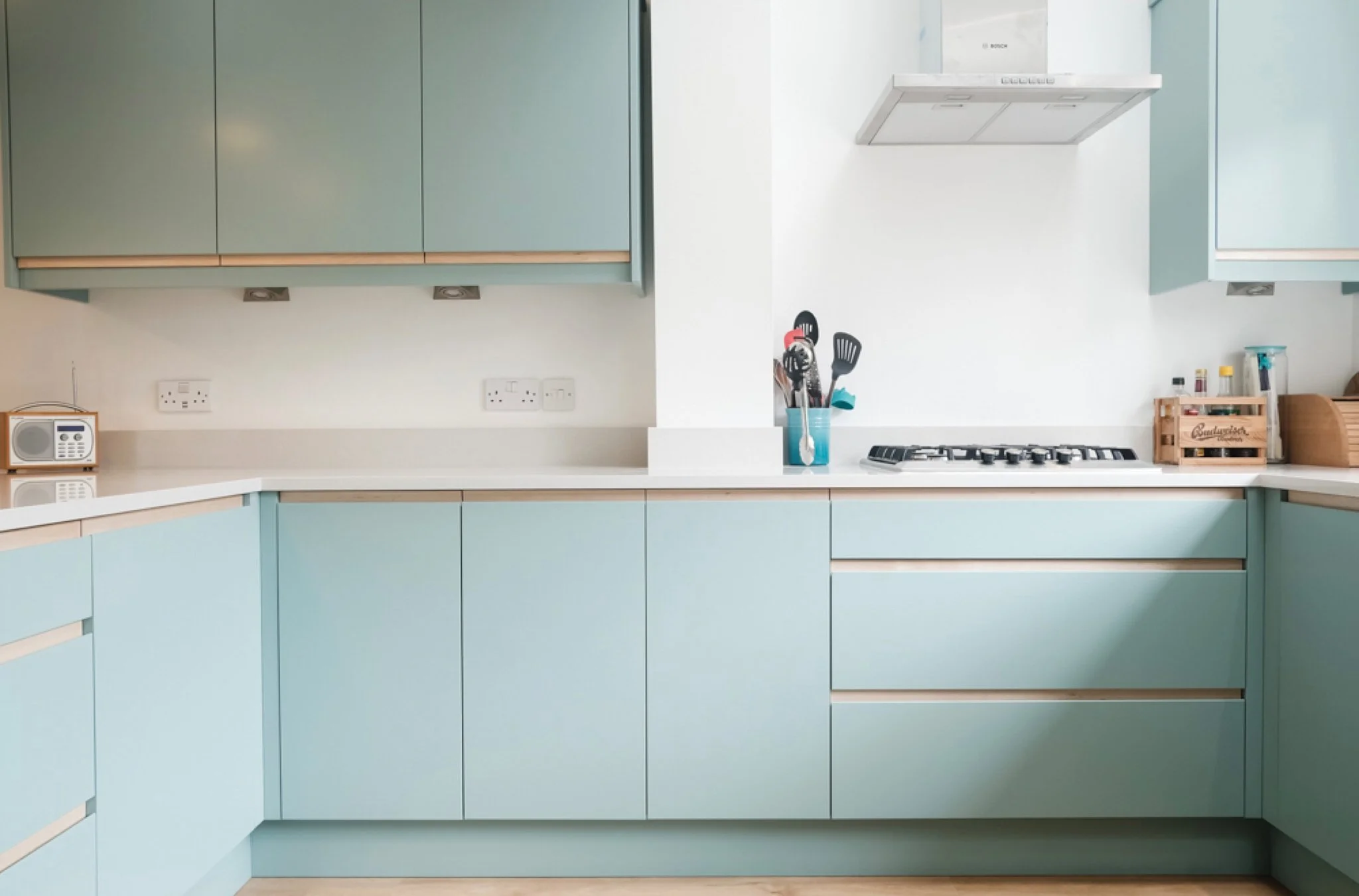 Modern kitchen with light blue cabinets, white countertops, a gas stove, a range hood, and kitchen utensils in a holder.