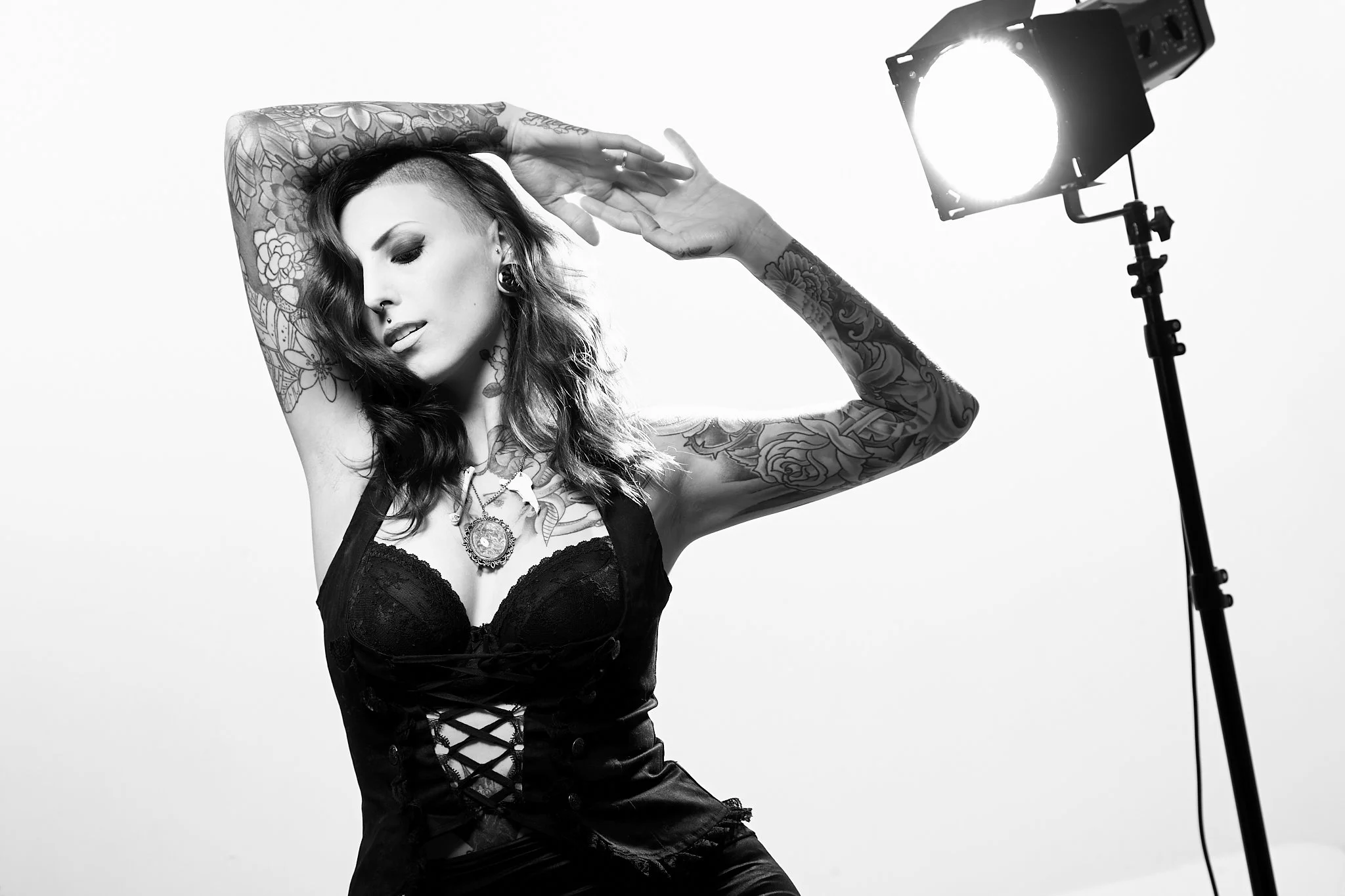 A tattooed woman in a black lace top posing in a studio with professional lighting, black and white photo.