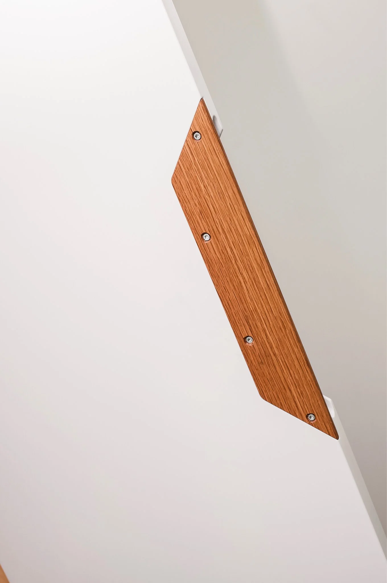 Close-up of a ceiling corner with a wooden ventilation panel attached with screws.