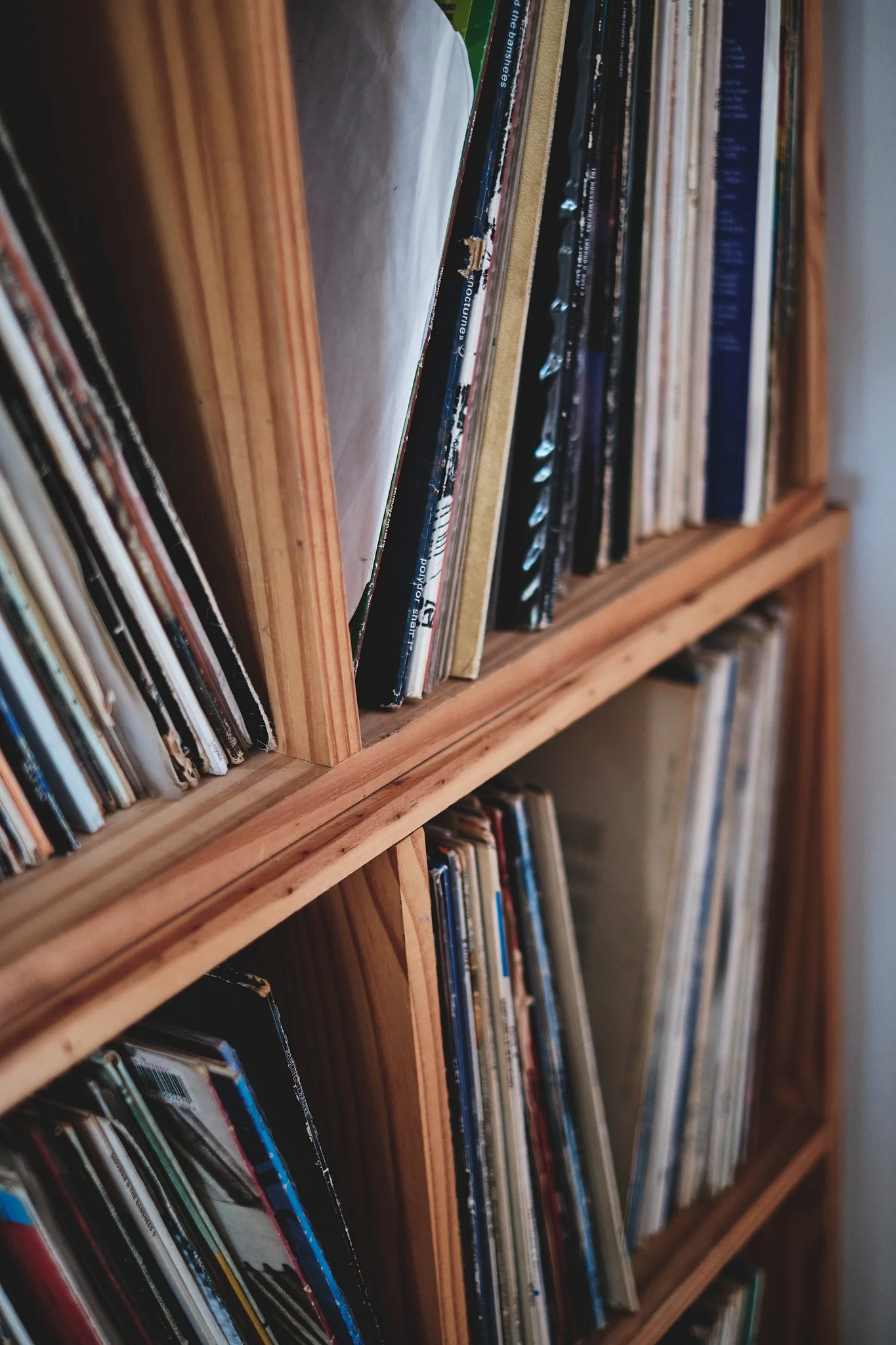 A wooden bookshelf filled with vinyl records and albums, some leaning and stacked.