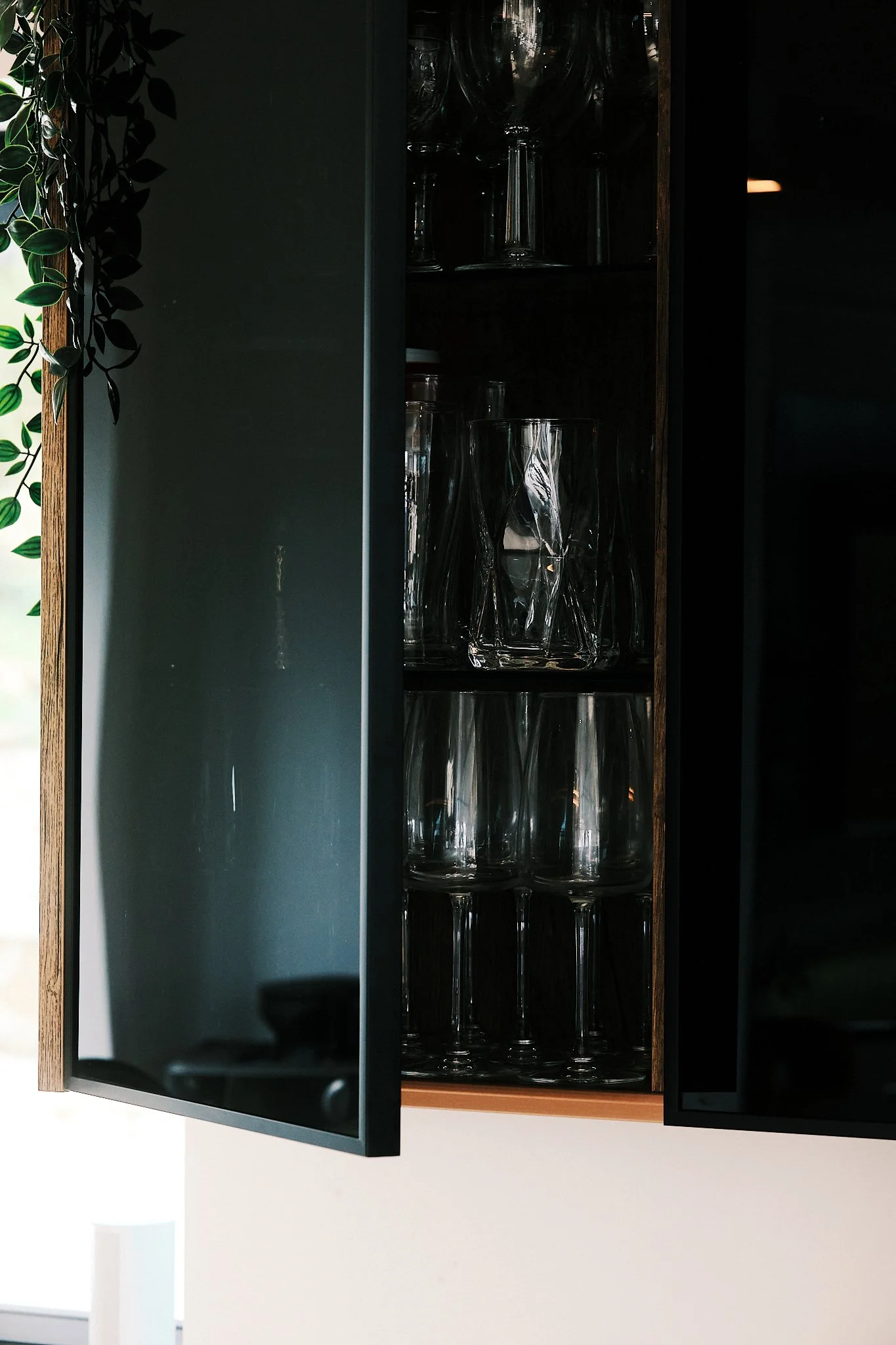 A partially open glass cabinet filled with upside-down drinking glasses, with a dark interior and a black door.