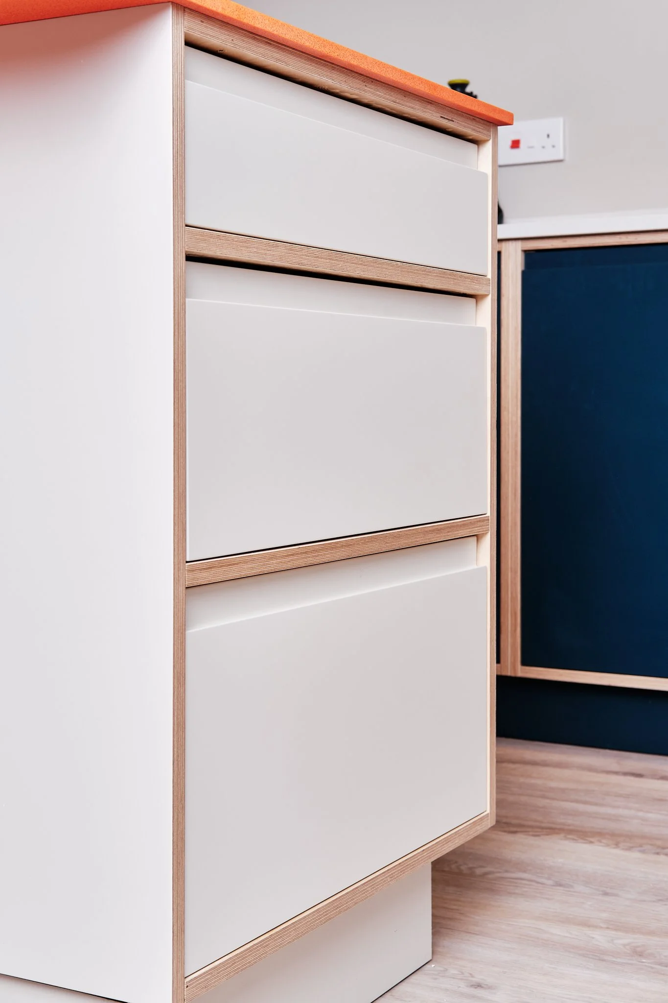 Modern kitchen drawer unit with three white drawers and a wooden frame.