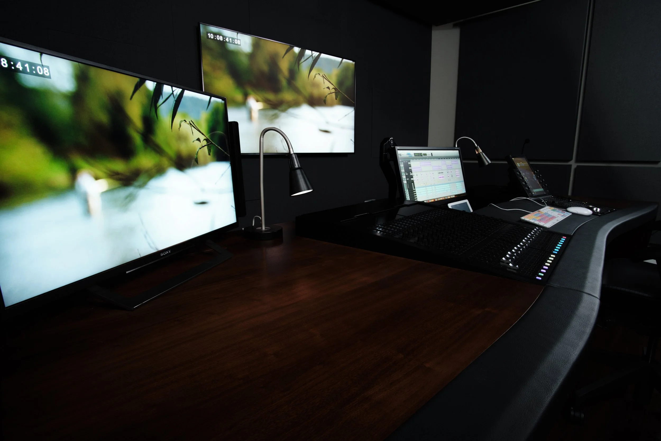 A modern audio or video production studio with multiple monitors and a mixing console on a wooden desk.