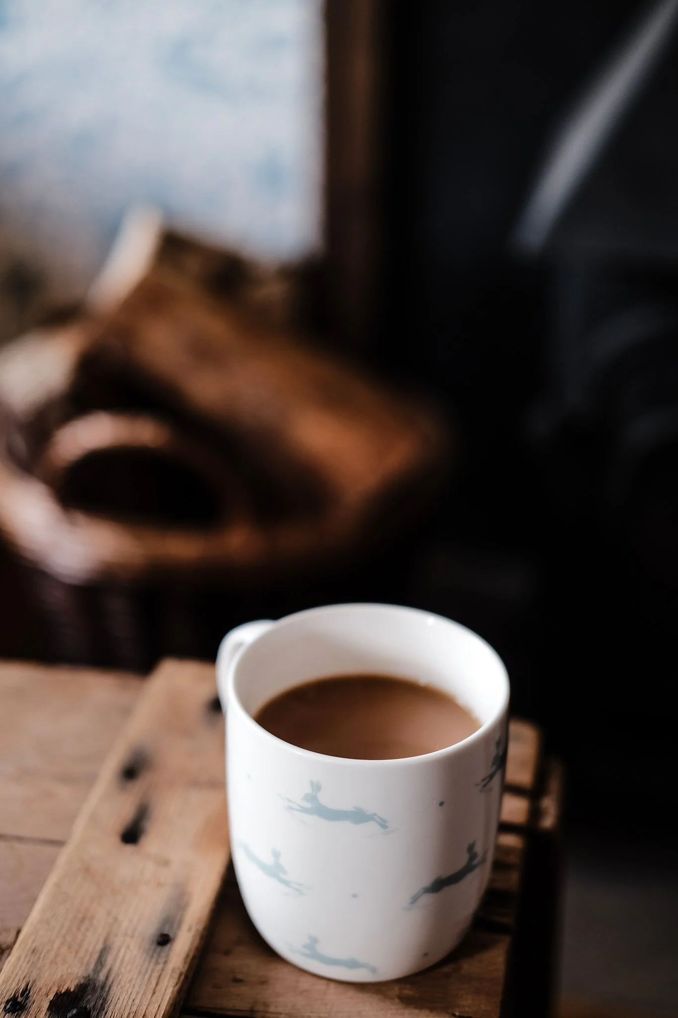 A white mug with flamingo prints filled with coffee on a wooden surface in a cozy setting, with blurred background.
