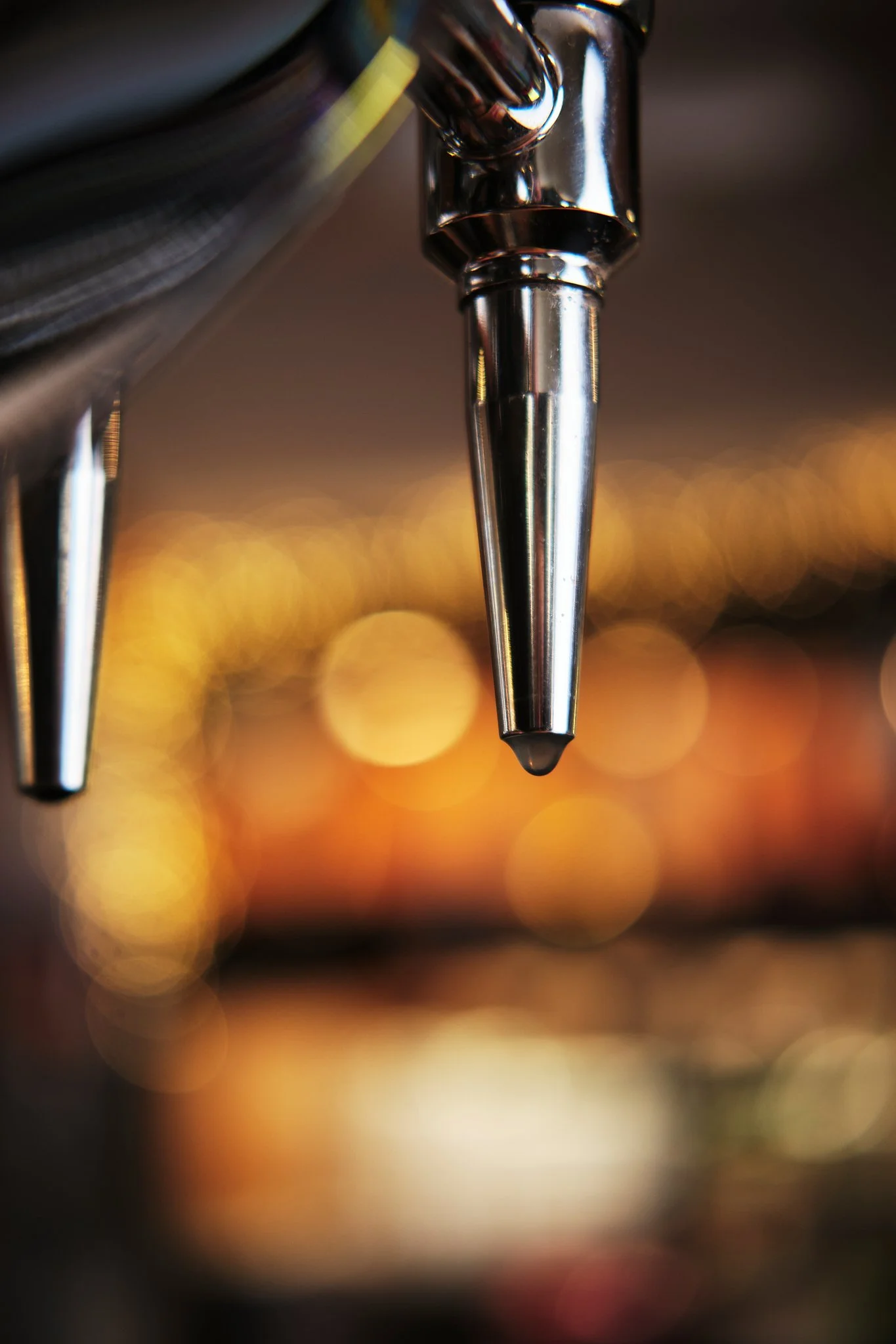 Close-up of coffee machine spout with blurred colorful lights in the background.