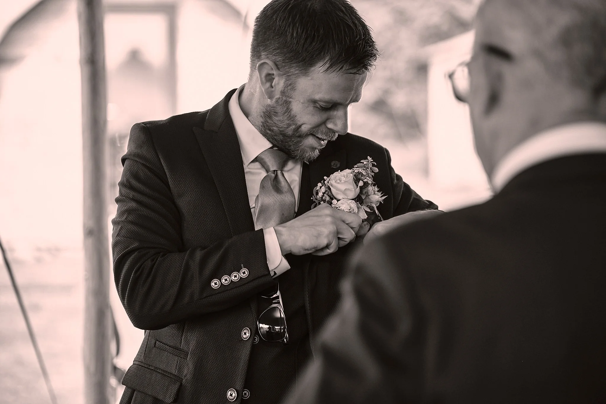 A man in a suit pinning a boutonniere on another person's jacket during a formal event.