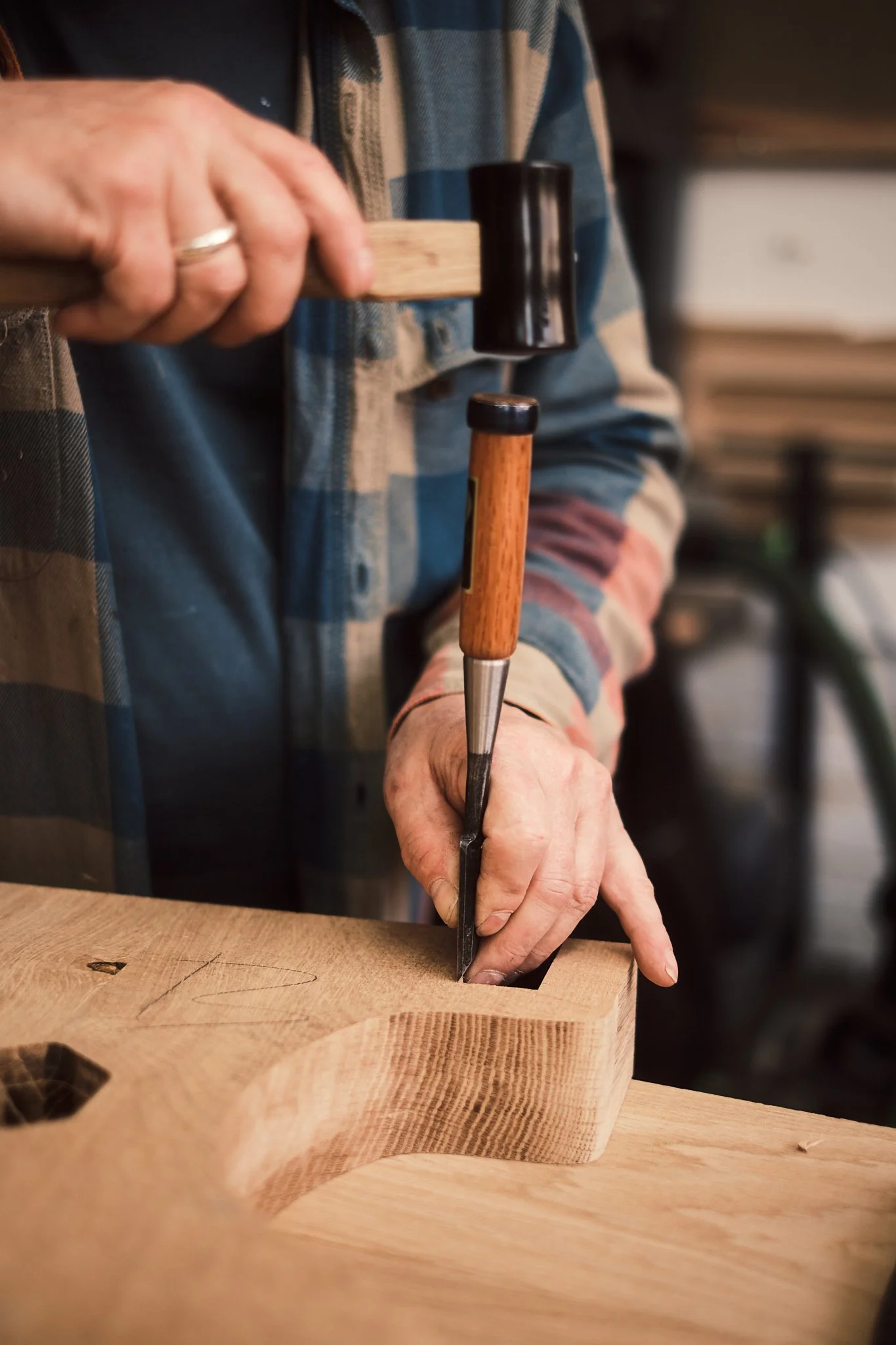 Person carving a heart shape into a piece of wood with a chisel and hammer.