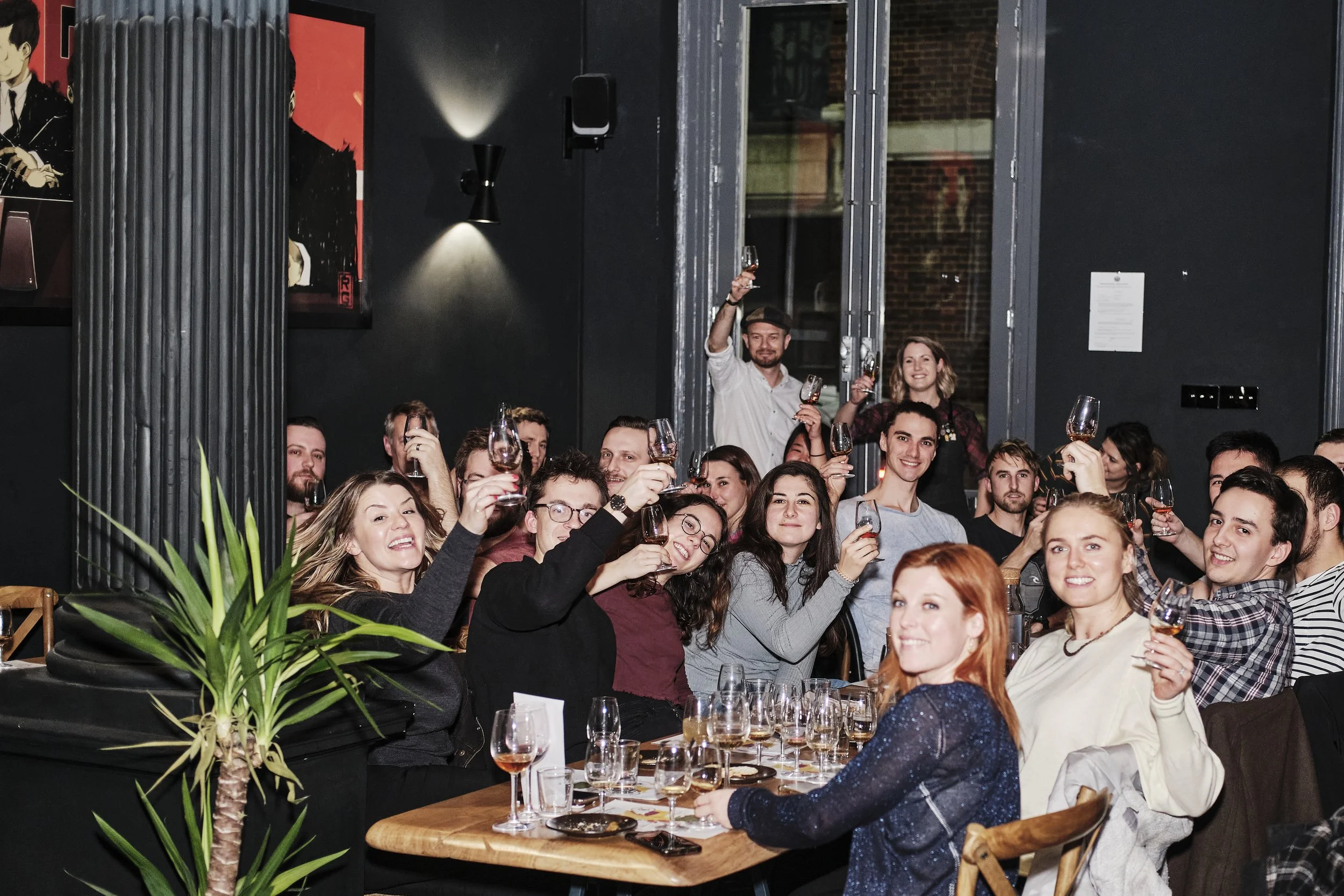 Group of people celebrating at a restaurant or bar, raising wine glasses for a toast.