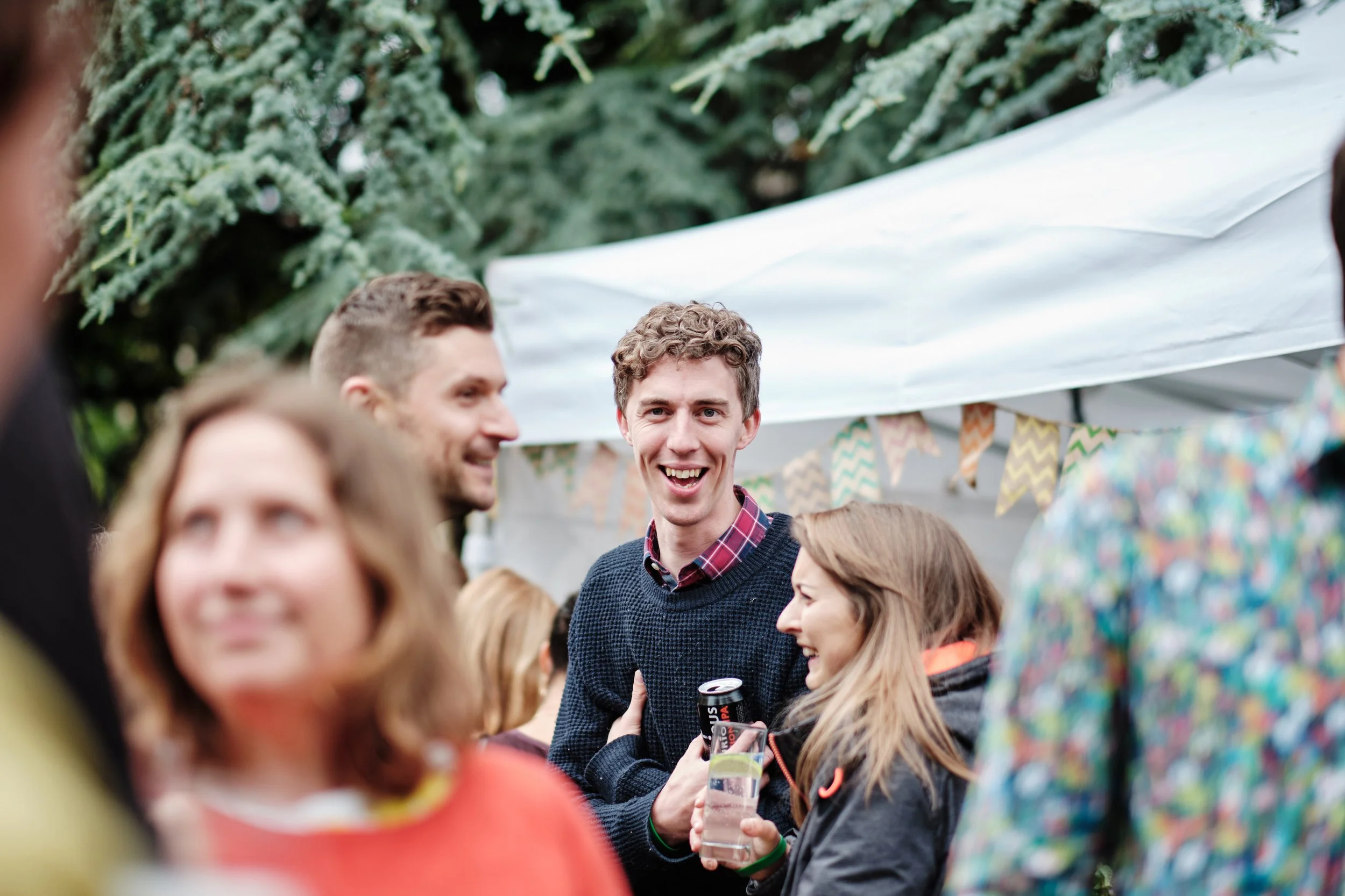 People gathered at an outdoor event, smiling and talking, with a tent and festive bunting in the background.