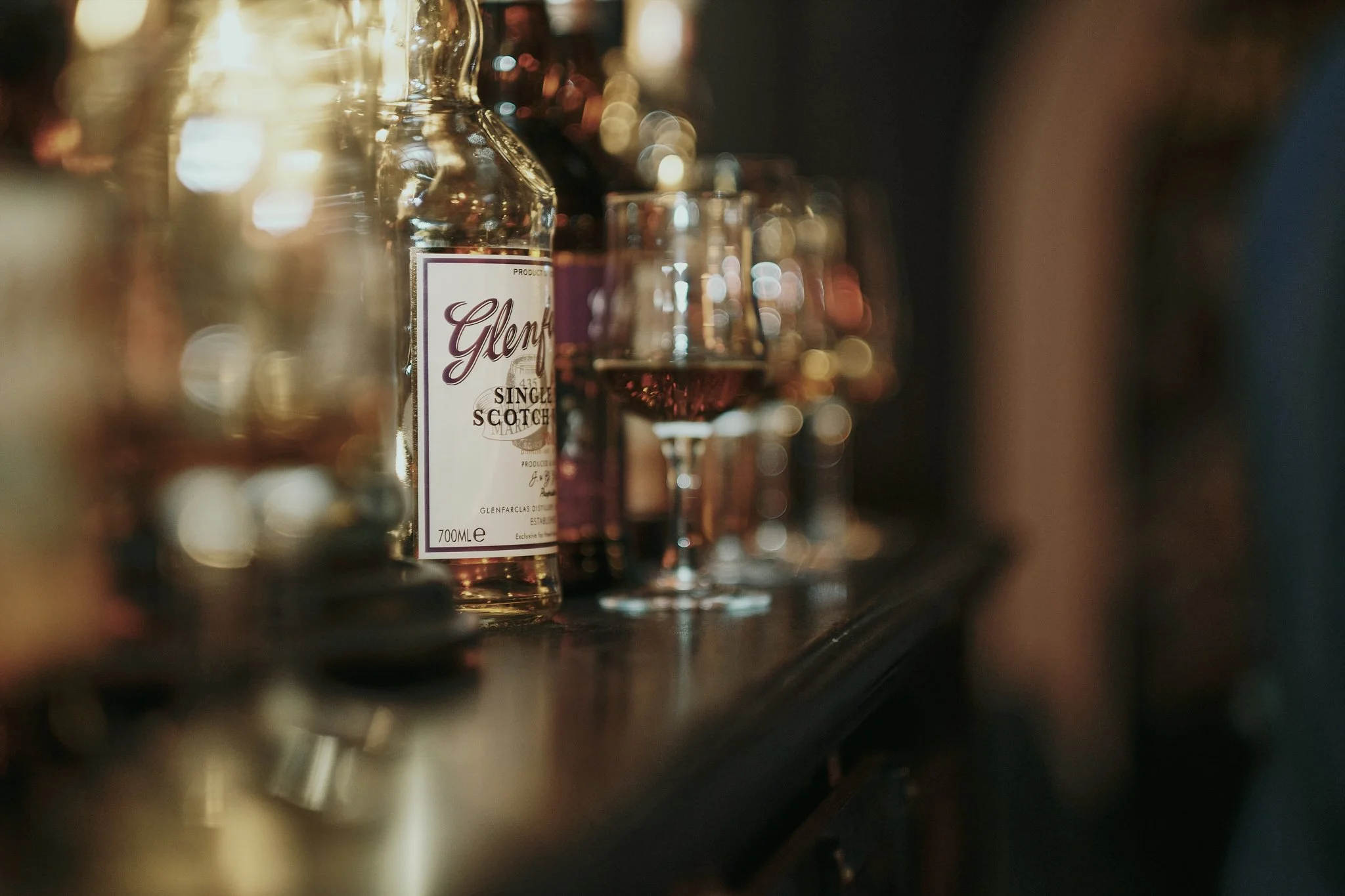 A bottle of Glenfiddich single malt Scotch whisky and a glass of whisky on a bar counter.