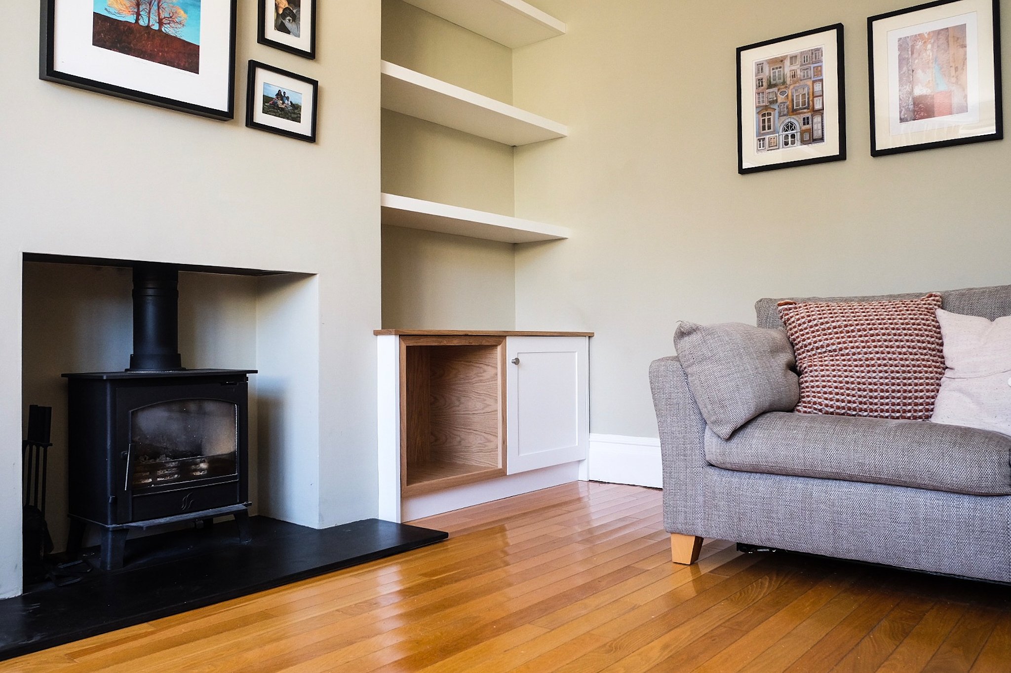 Living room with a gray couch, patterned pillows, a black wood stove, and framed artwork on the walls.