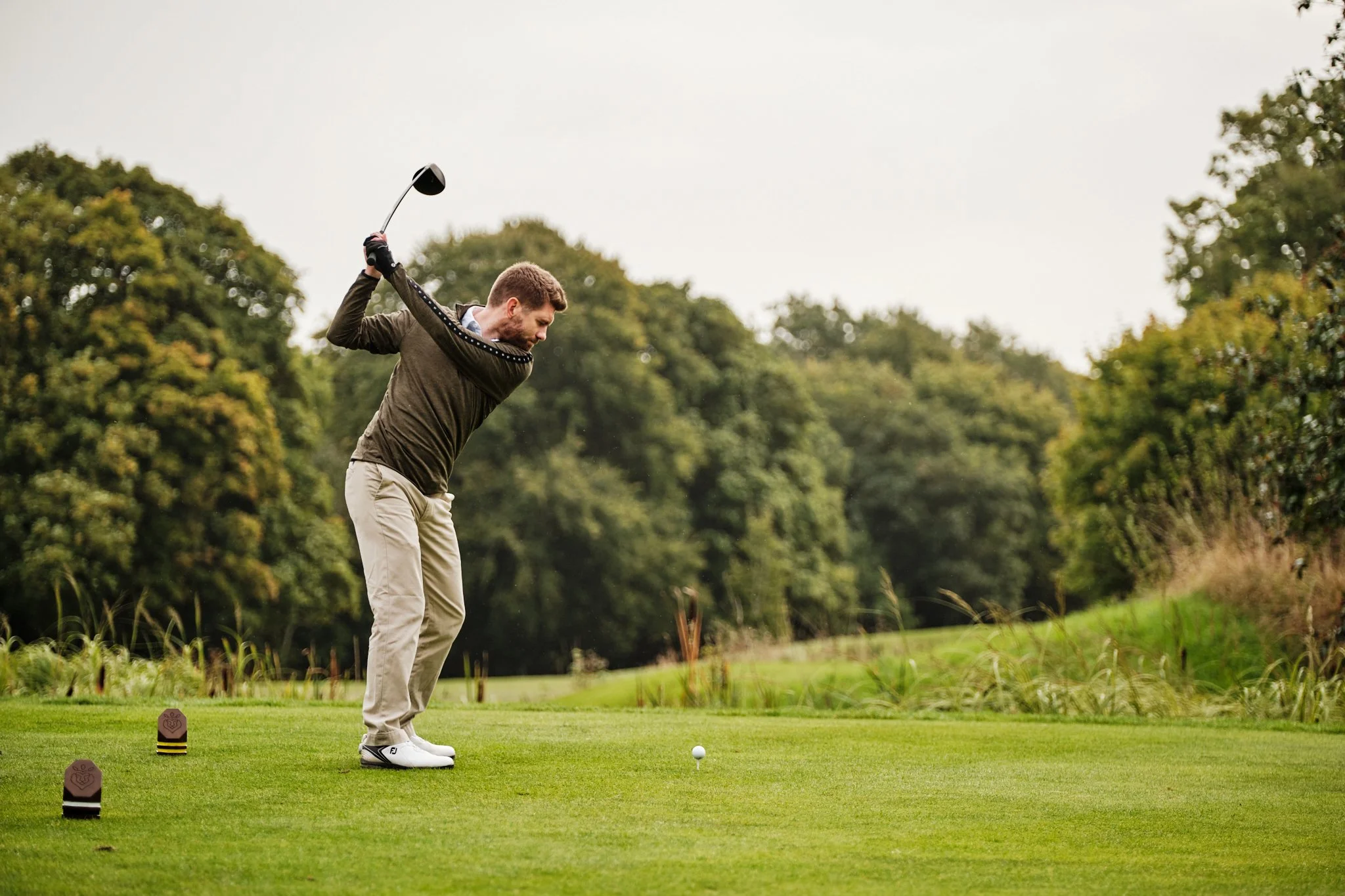 A man teeing off a golf ball on a golf course, surrounded by trees and greenery.