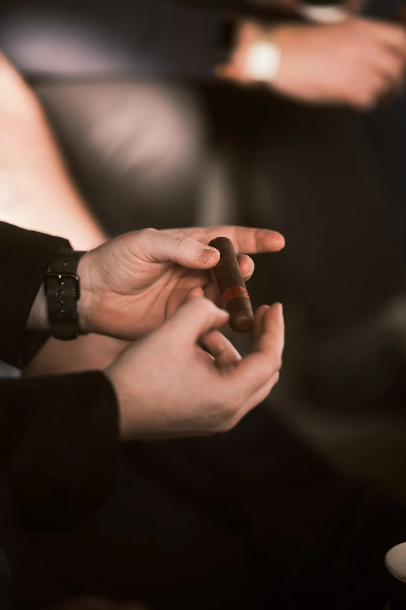 Person holding a cigar in their hand, wearing a black sleeve and a black wristwatch.