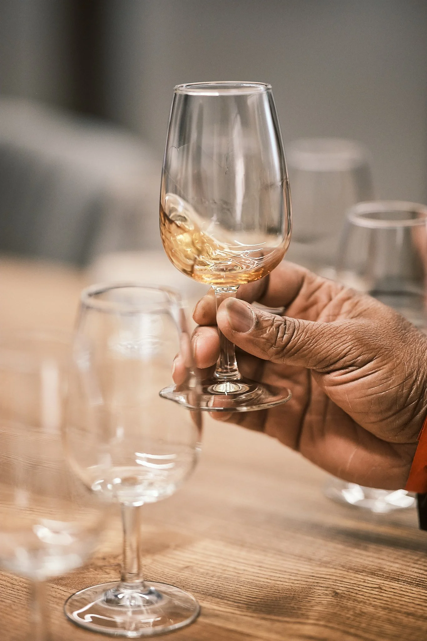 A hand holding a glass of rosé wine above a wooden table with other empty wine glasses.