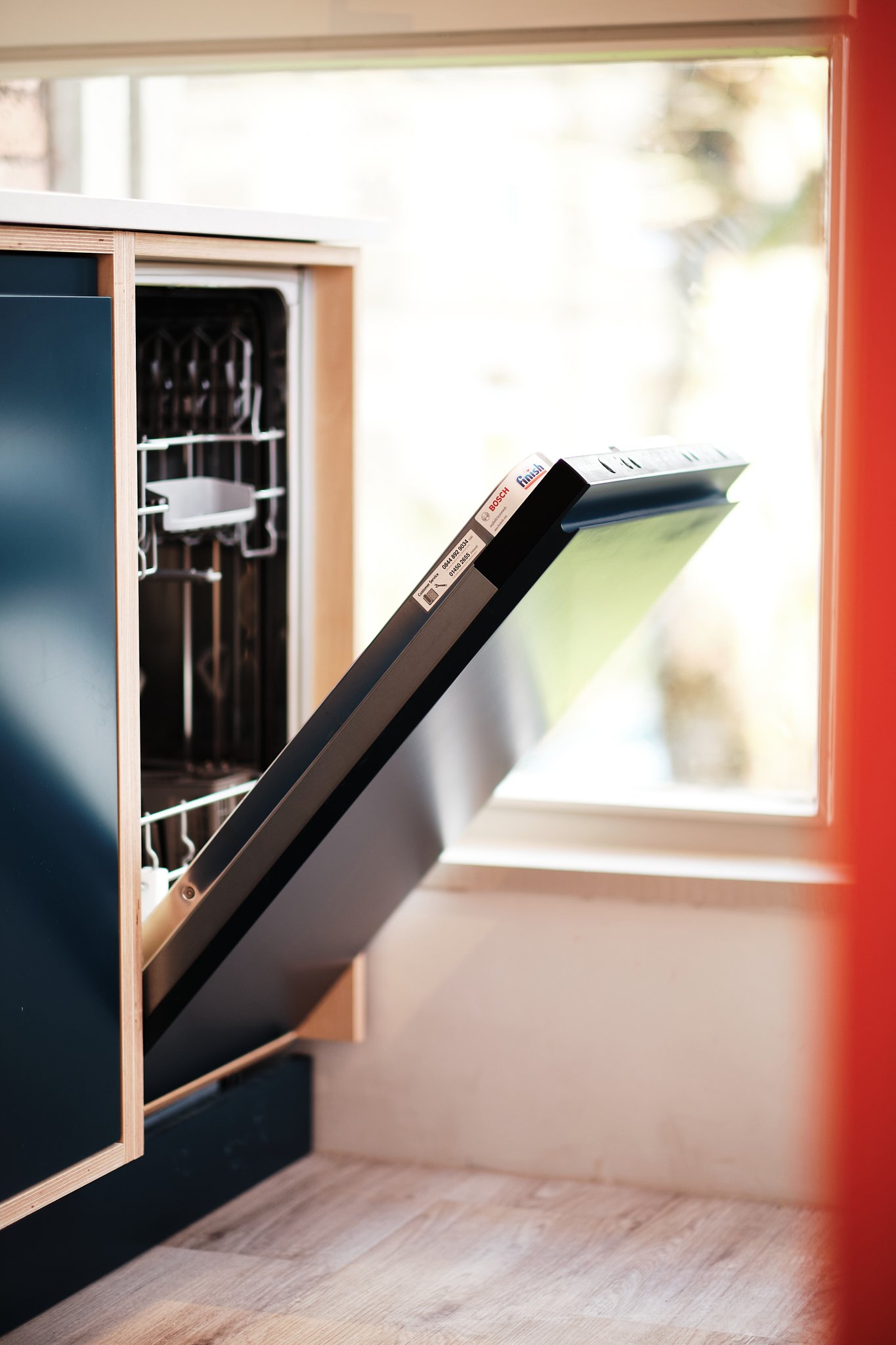 Partially open dishwasher in a kitchen next to a window with sunlight.