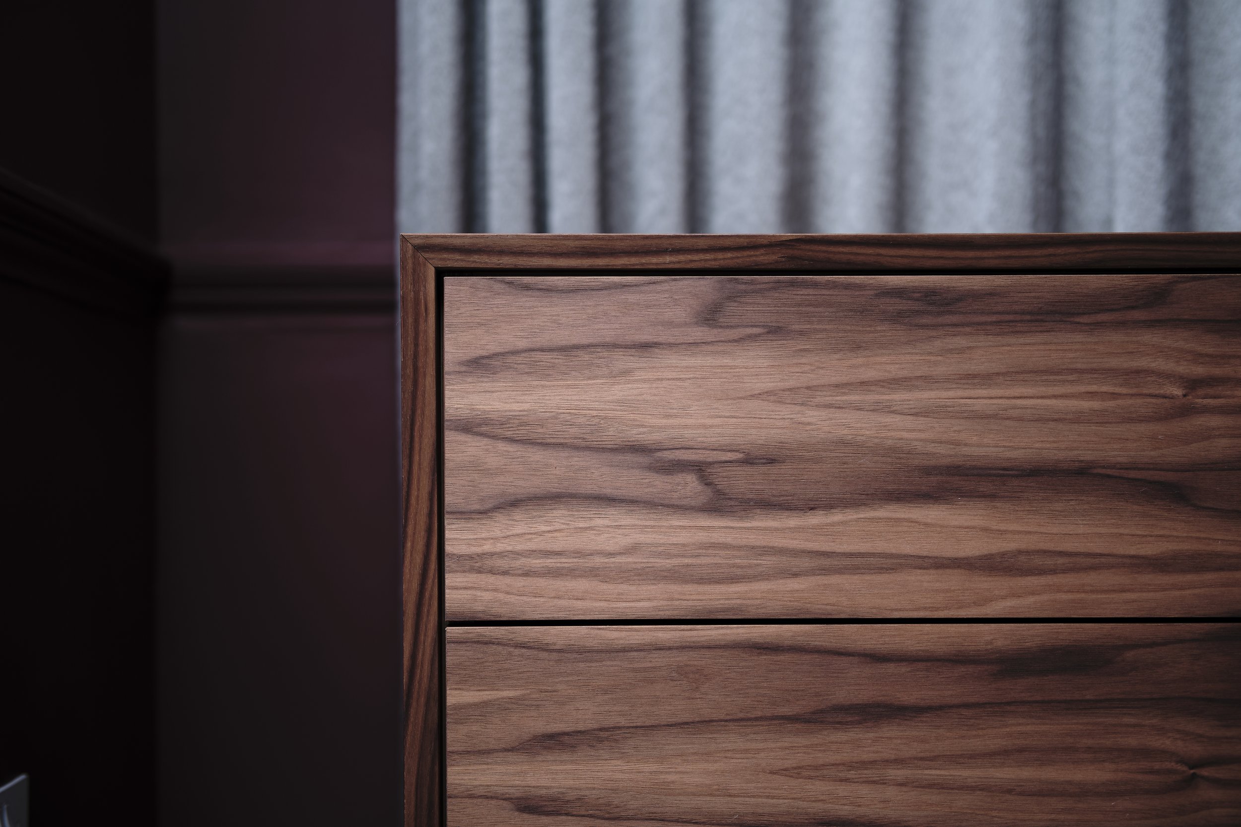 Close-up of a wooden dresser with a woodgrain finish, set against a wall with curtains in the background.