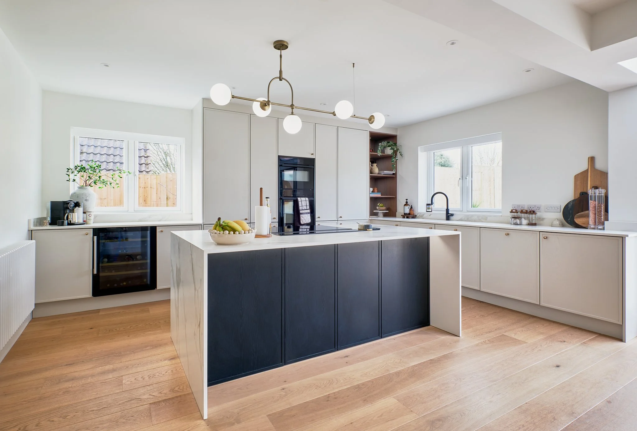 Modern kitchen with white cabinets, a black and white island, wooden floors, and large windows bringing in natural light.
