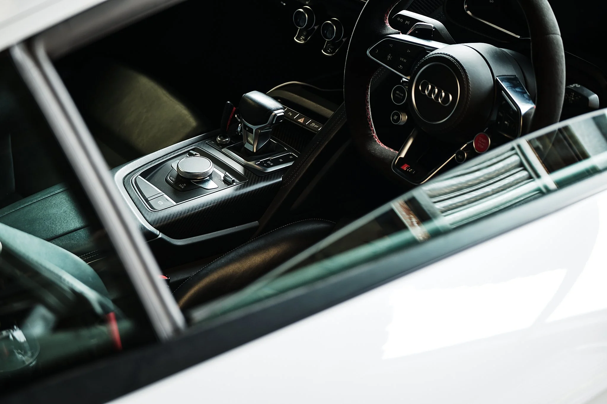 Interior of a luxury car showing a black steering wheel with the Audi logo, a gear shift, and a control knob on the center console.