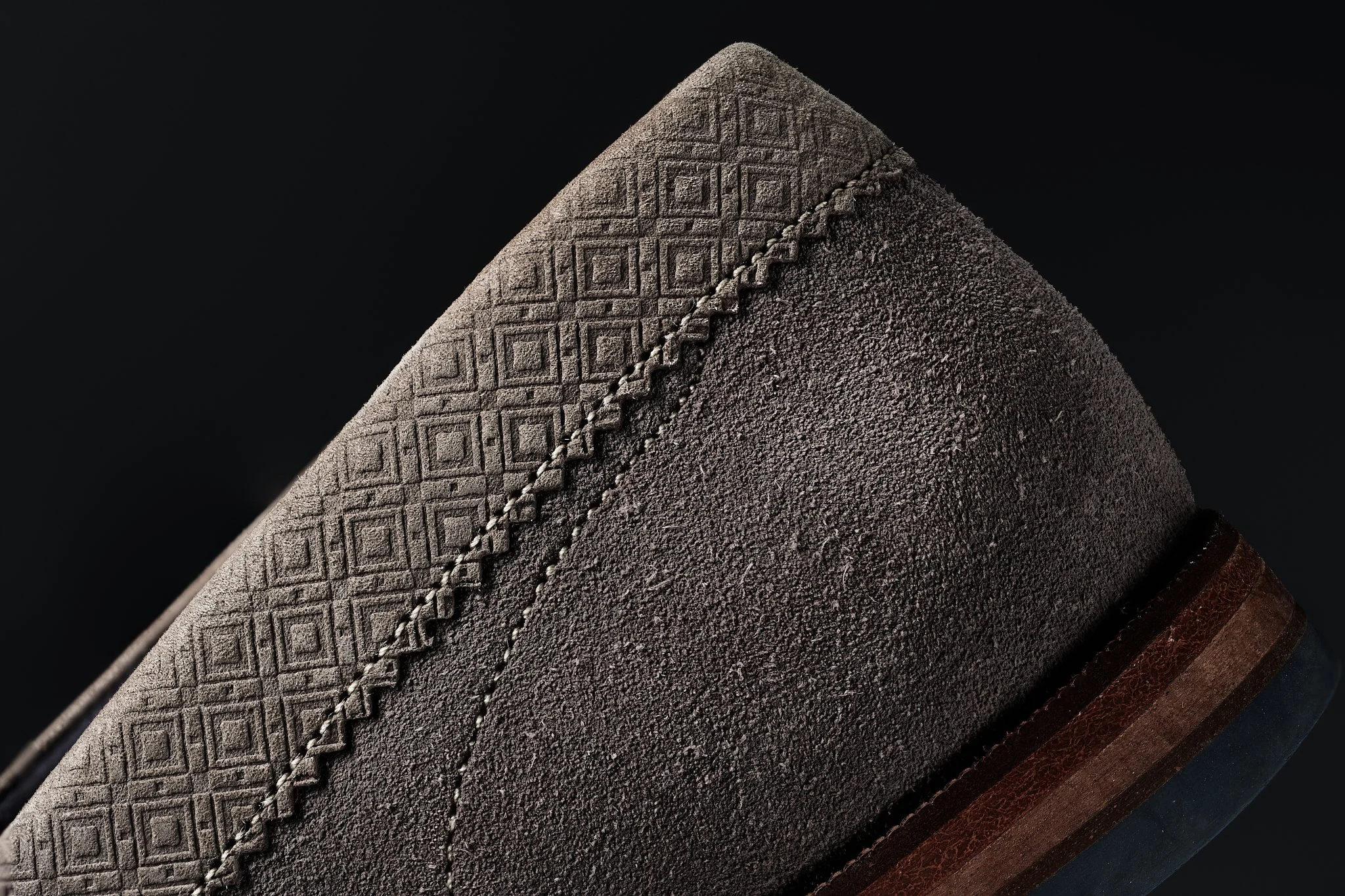 Close-up of the sole of a brown leather dress shoe, showing detailed textured and stitched design against a black background.