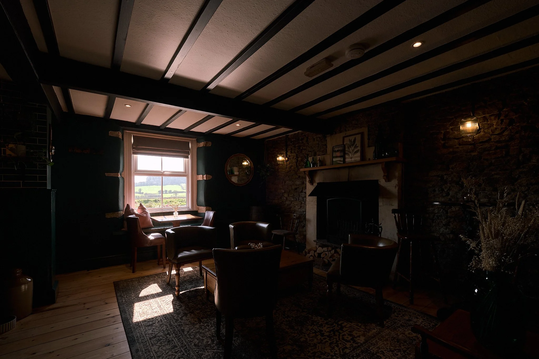 Cozy living room with a window view of a rural landscape, a stone fireplace, leather chairs, and warm lighting.