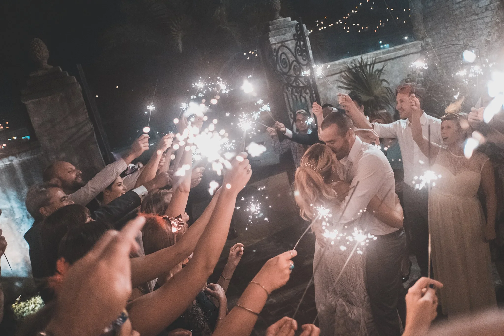 People celebrating with sparklers at night, smiling and holding sparklers above their heads in a lively gathering.