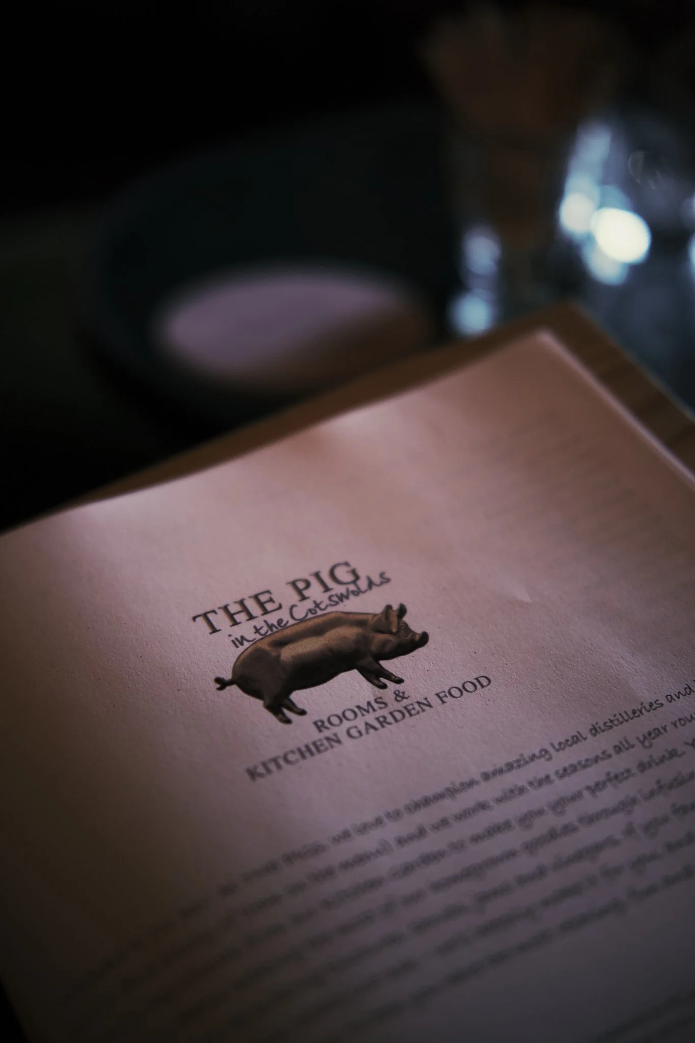 Close-up of a menu titled 'The Pig in the Counting Rooms & Kitchen Garden Food' with a pig illustration, in a dimly lit setting. Hotel interior photography at THE PIG-in the Cotswolds