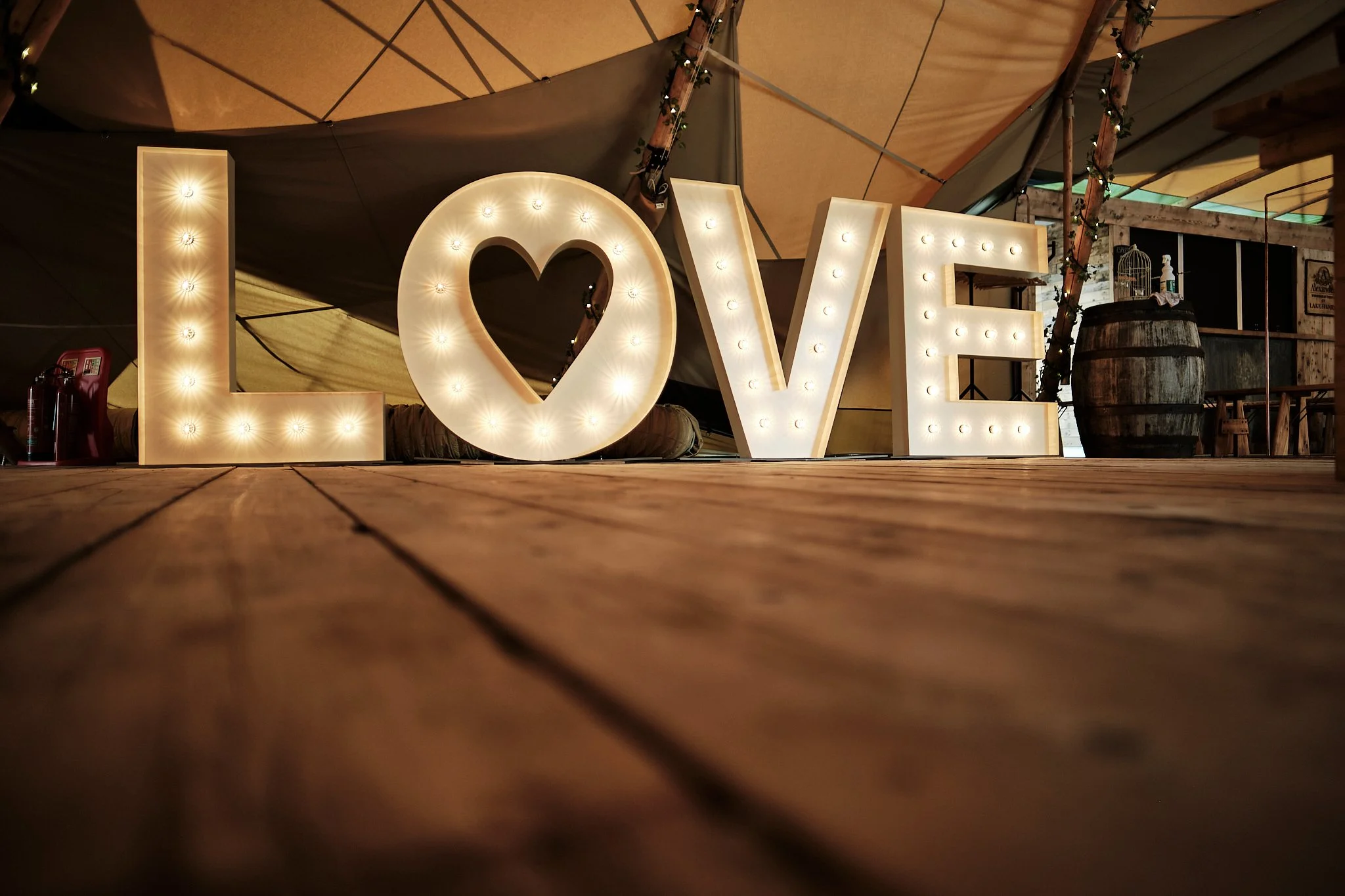Illuminated marquee letters spelling out the word 'LOVE' on a wooden floor in a rustic setting.