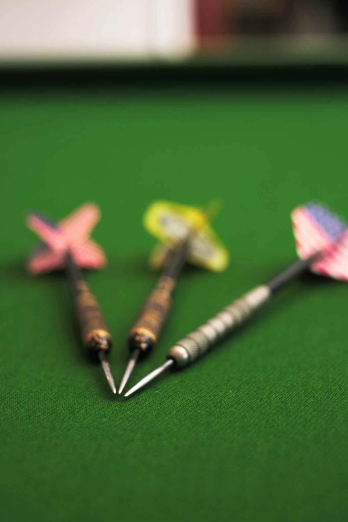 Three darts with colorful flights placed on a green surface, with blurred background.