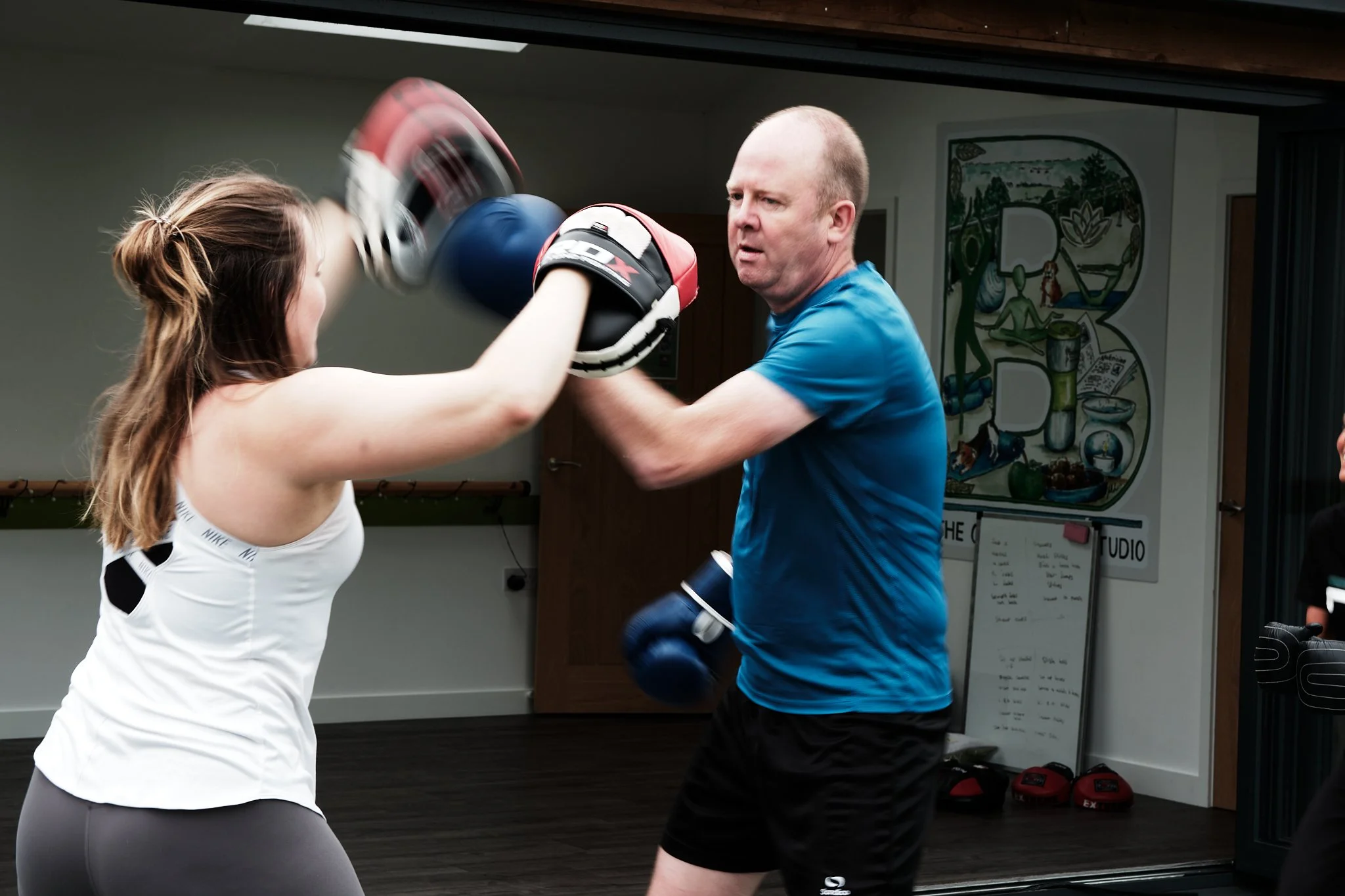 A woman practicing boxing punches with a trainer at a gym, with both wearing boxing gloves.