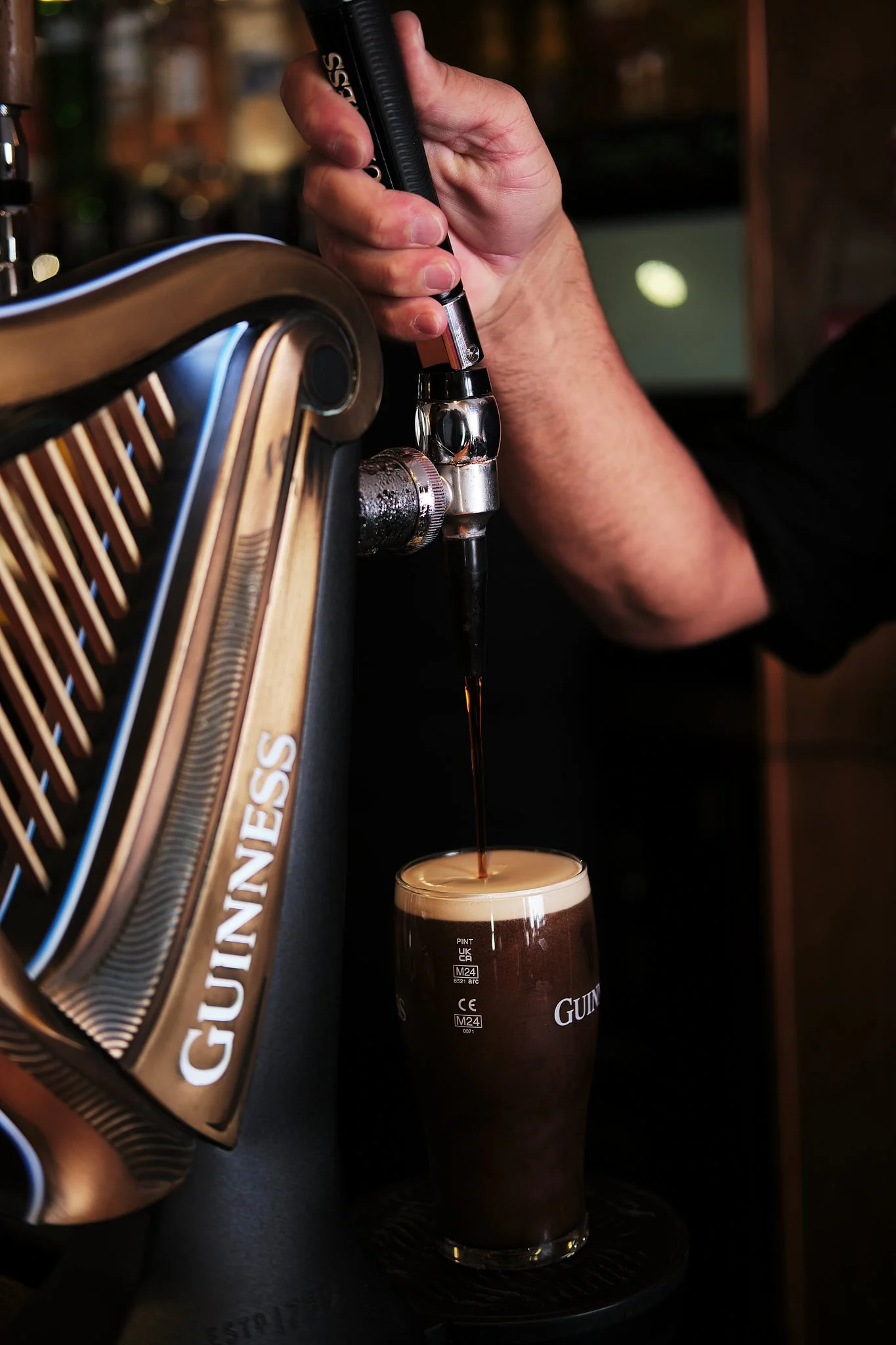 A person pours Guinness beer from a tap into a glass.