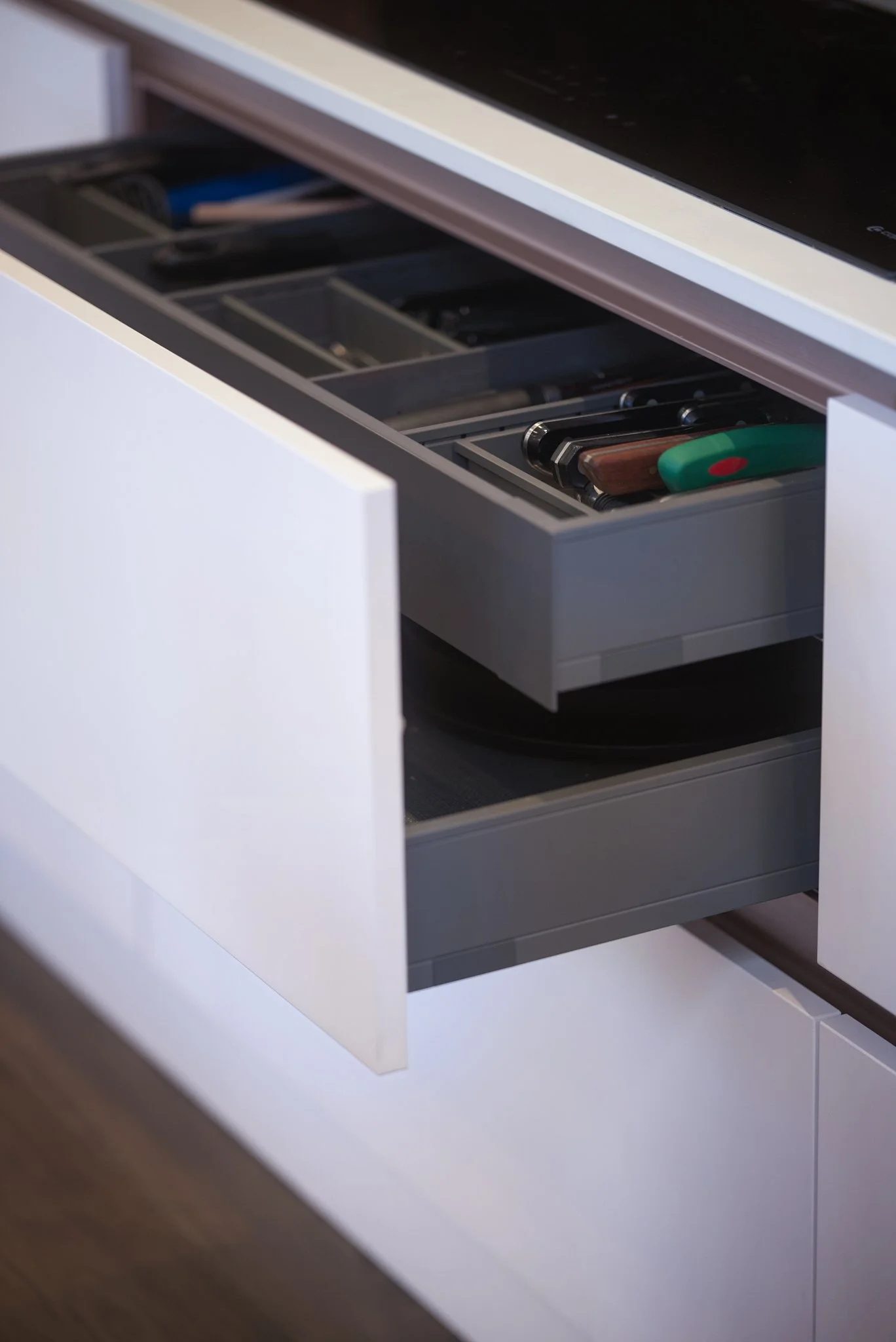 Kitchen drawer with various kitchen tools, including a spatula, a wooden spoon, and a green bottle opener.