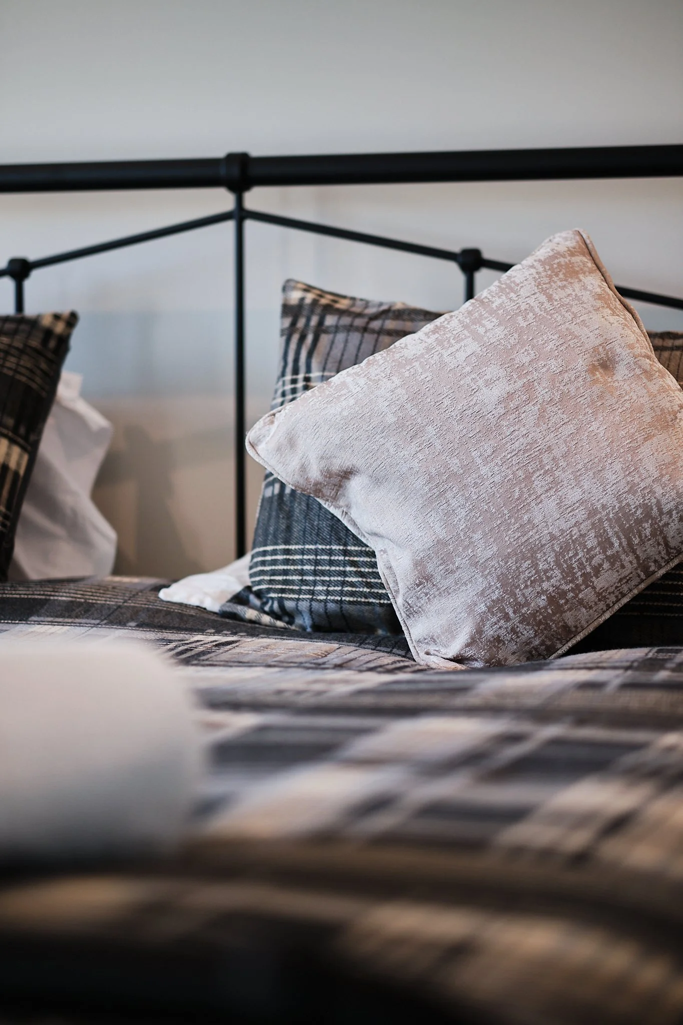 Close-up of a bed with plaid and solid-colored pillows against a black metal headboard.