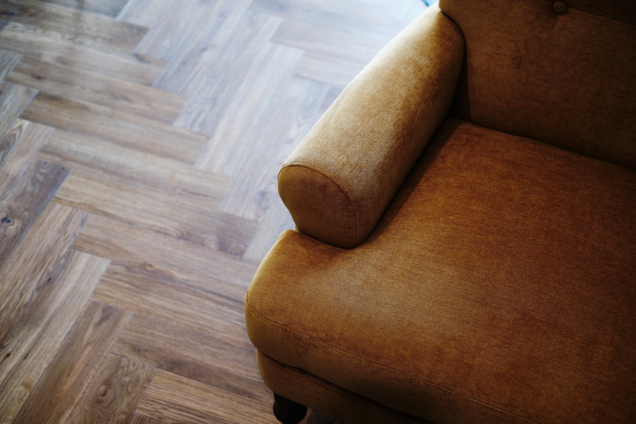 Close-up of a mustard-colored upholstered sofa with rolled armrest on a wooden floor.