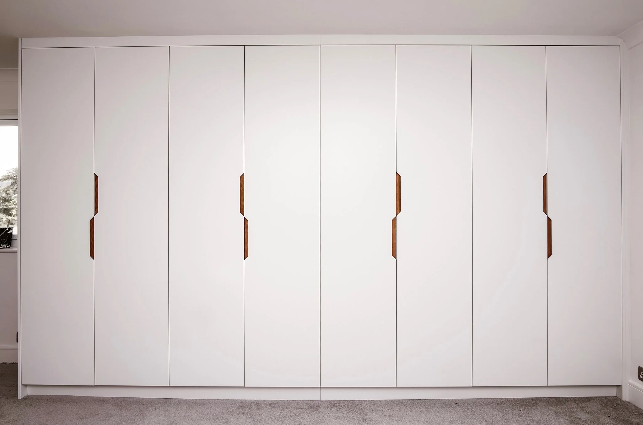White built-in wardrobe with patterned wooden handles in a minimal bedroom.