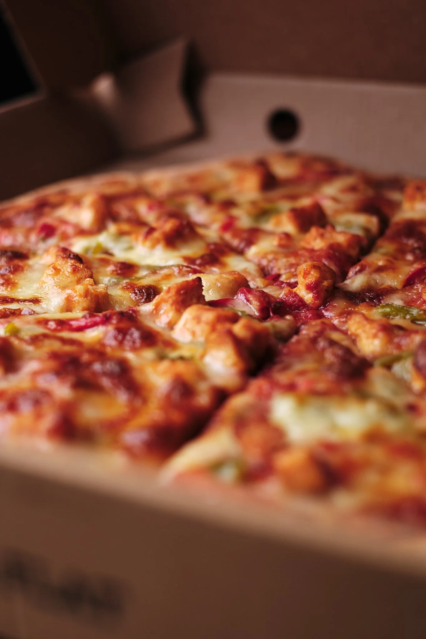 Close-up of a freshly baked pizza with cheese, chicken, and green peppers in an open pizza box.