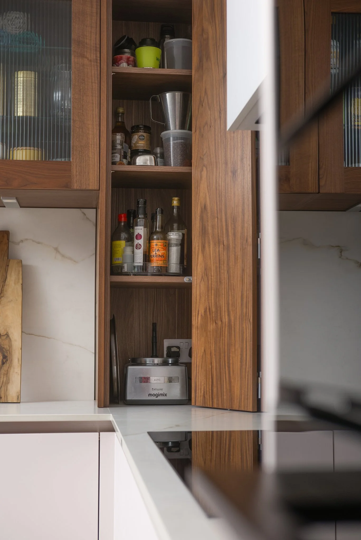 Open kitchen cabinet with various jars, bottles, and containers, with a countertop and a small kitchen appliance visible.