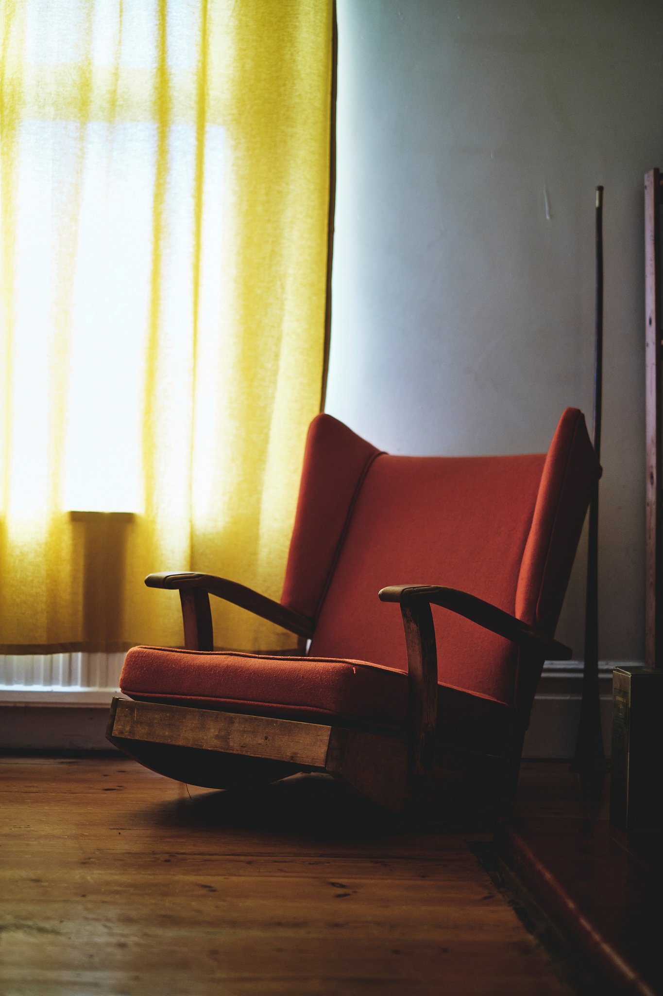 A vintage red armchair in front of yellow curtains with sunlight filtering through in a cozy room.
