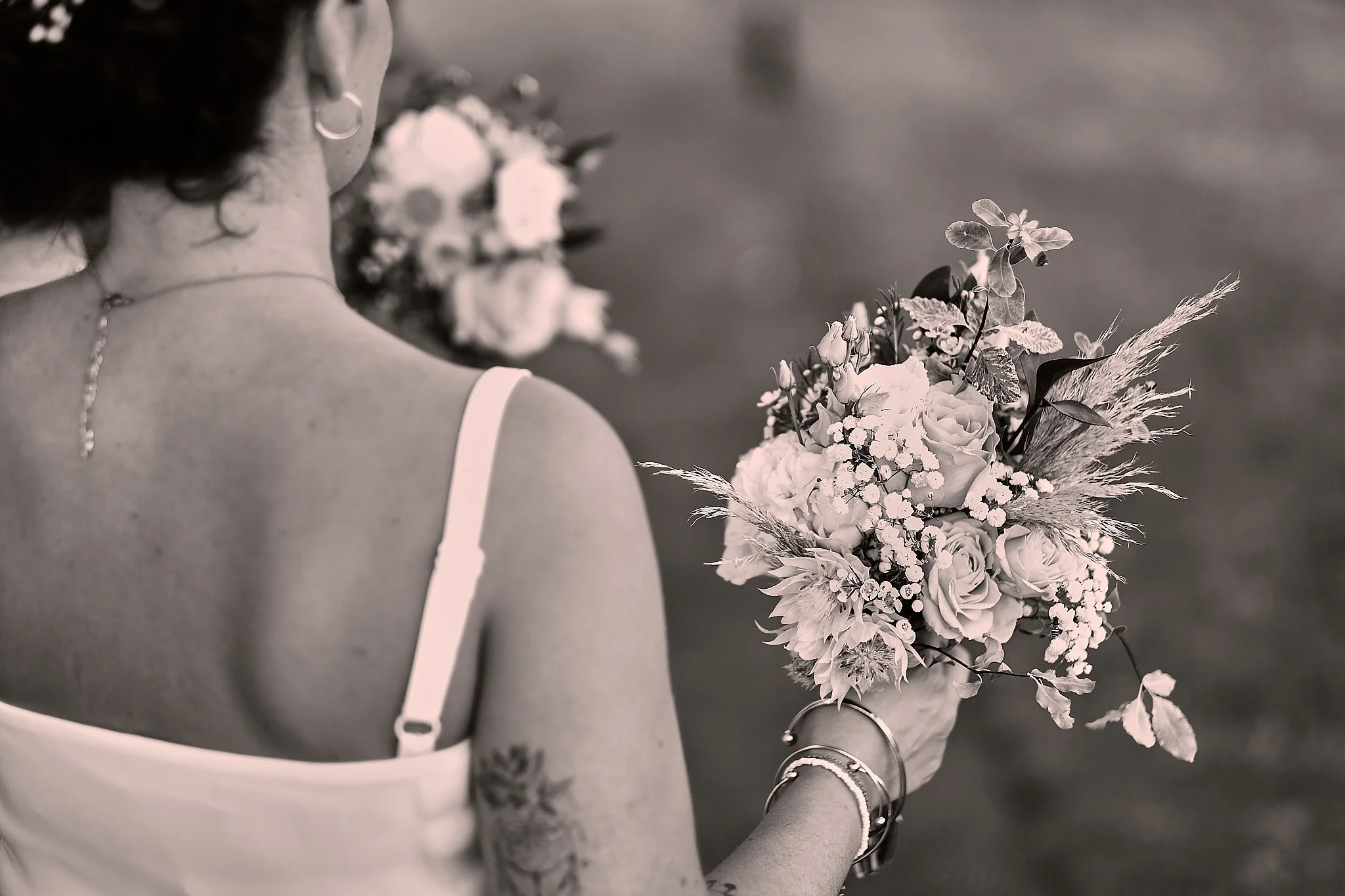 A person in a white dress holding a bouquet of flowers, seen from behind, in black and white.