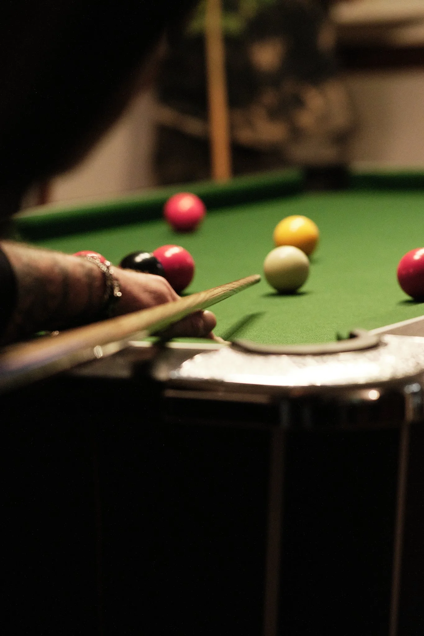 Person aiming a cue stick at billiard balls on a pool table in a dimly lit room.