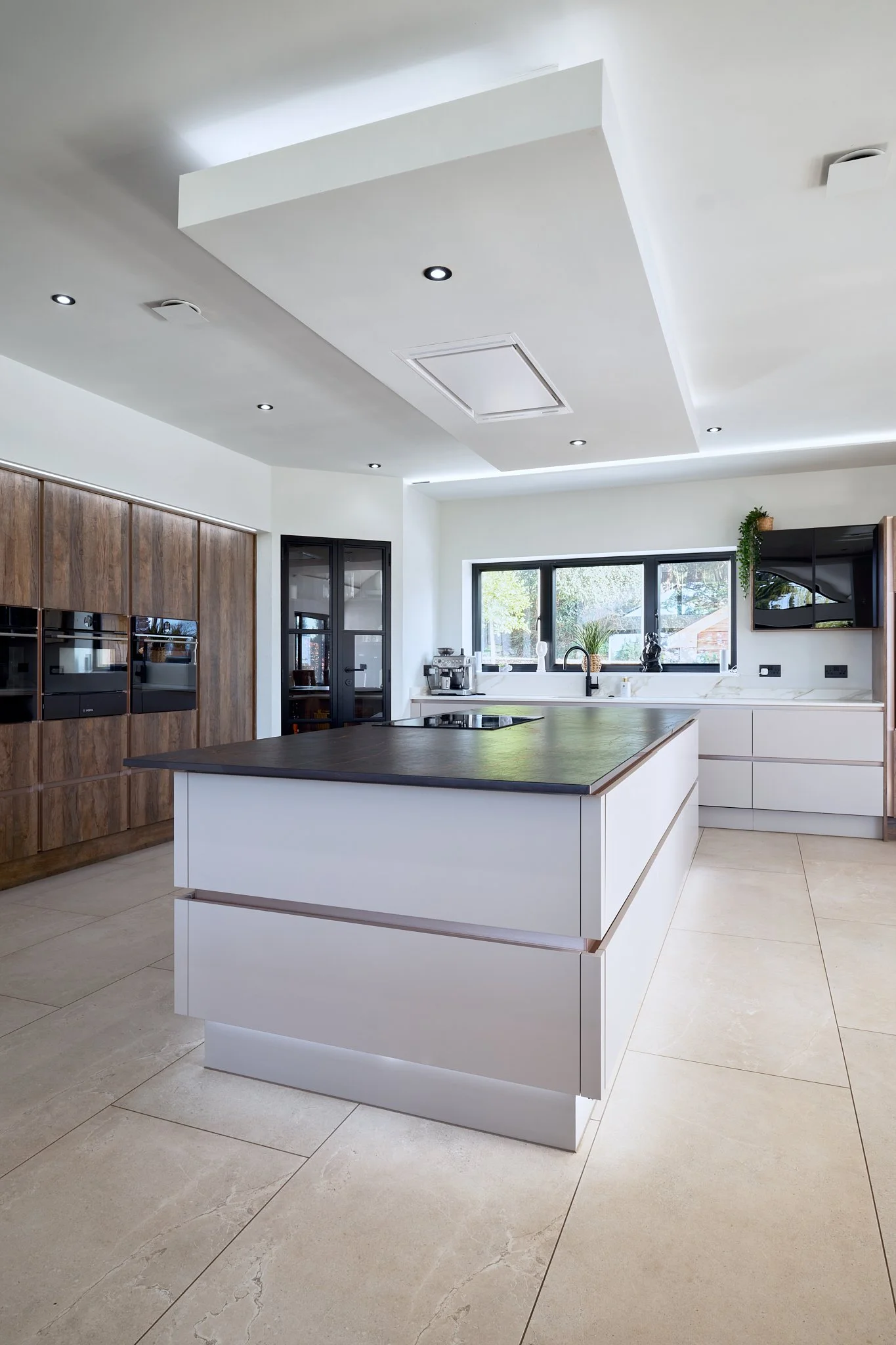 Modern kitchen with a central island, white cabinets, wooden wall cabinetry, a window above the sink, and ceiling lights.