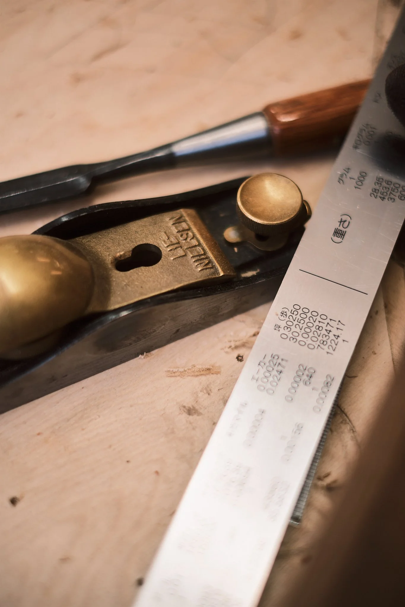 A carpenter's hand plane tool, a metal ruler, a chisel, and a paper receipt on a wooden surface.