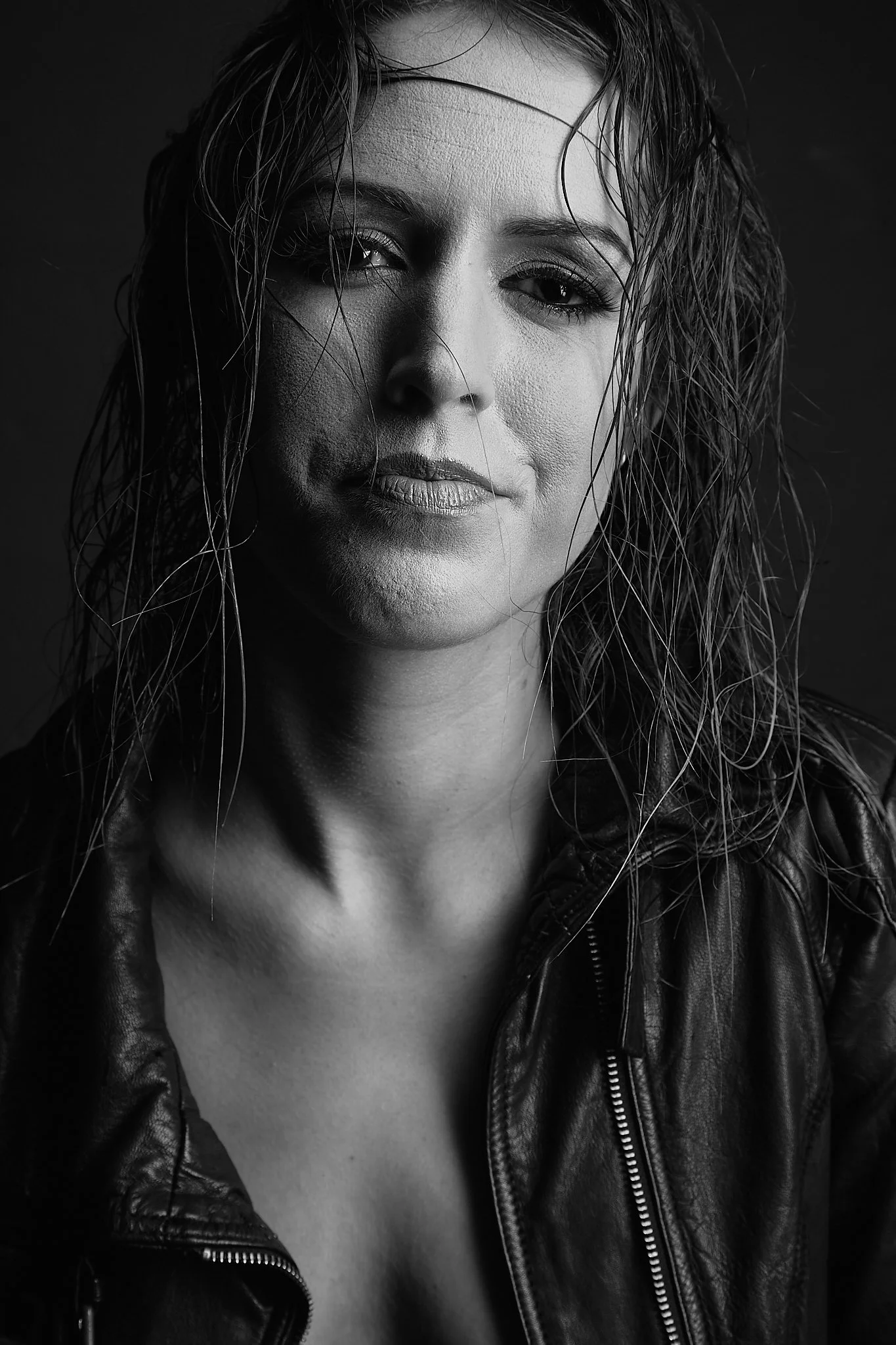 Black and white portrait of a woman with wet hair, wearing a leather jacket, looking at the camera with a serious expression.