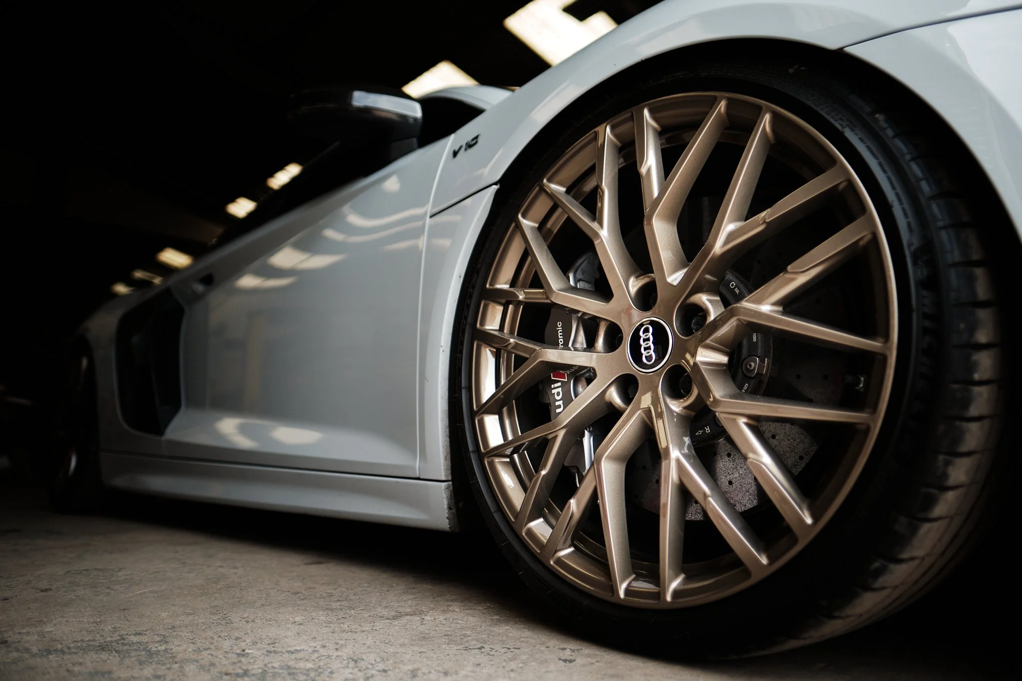 Close-up of a white Audi sports car with gold rims and brake calipers, parked indoors in a dimly lit environment.