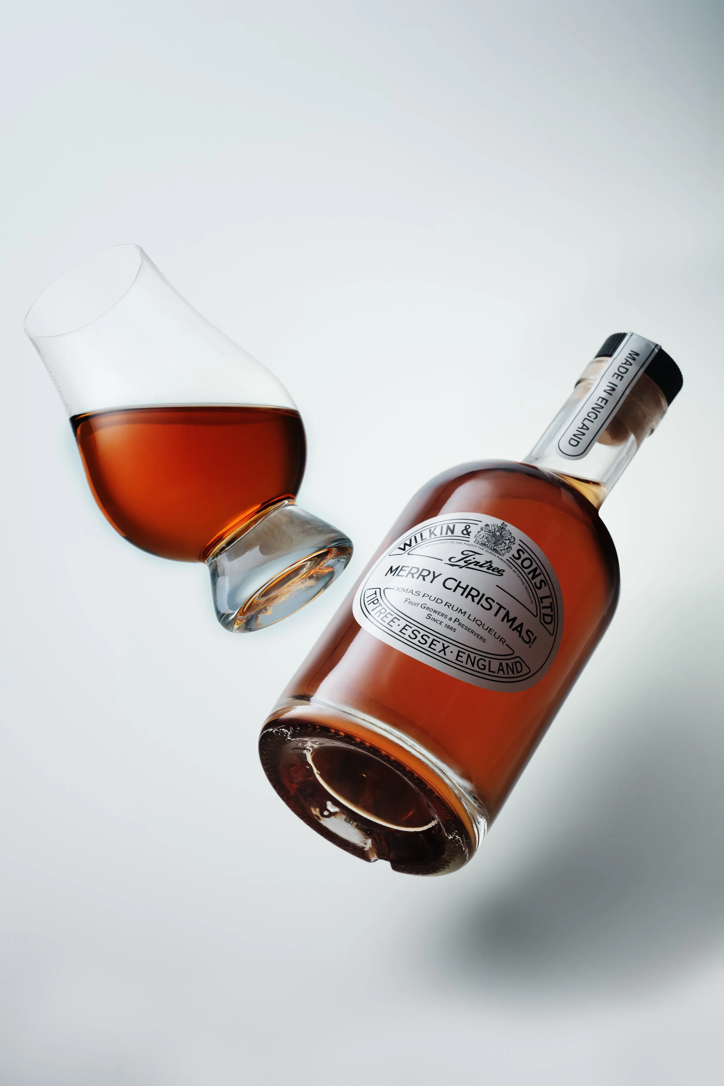 A glass of whisky and a bottle of Wilkin & Sons Merry Christmas whisky, both on a white background.