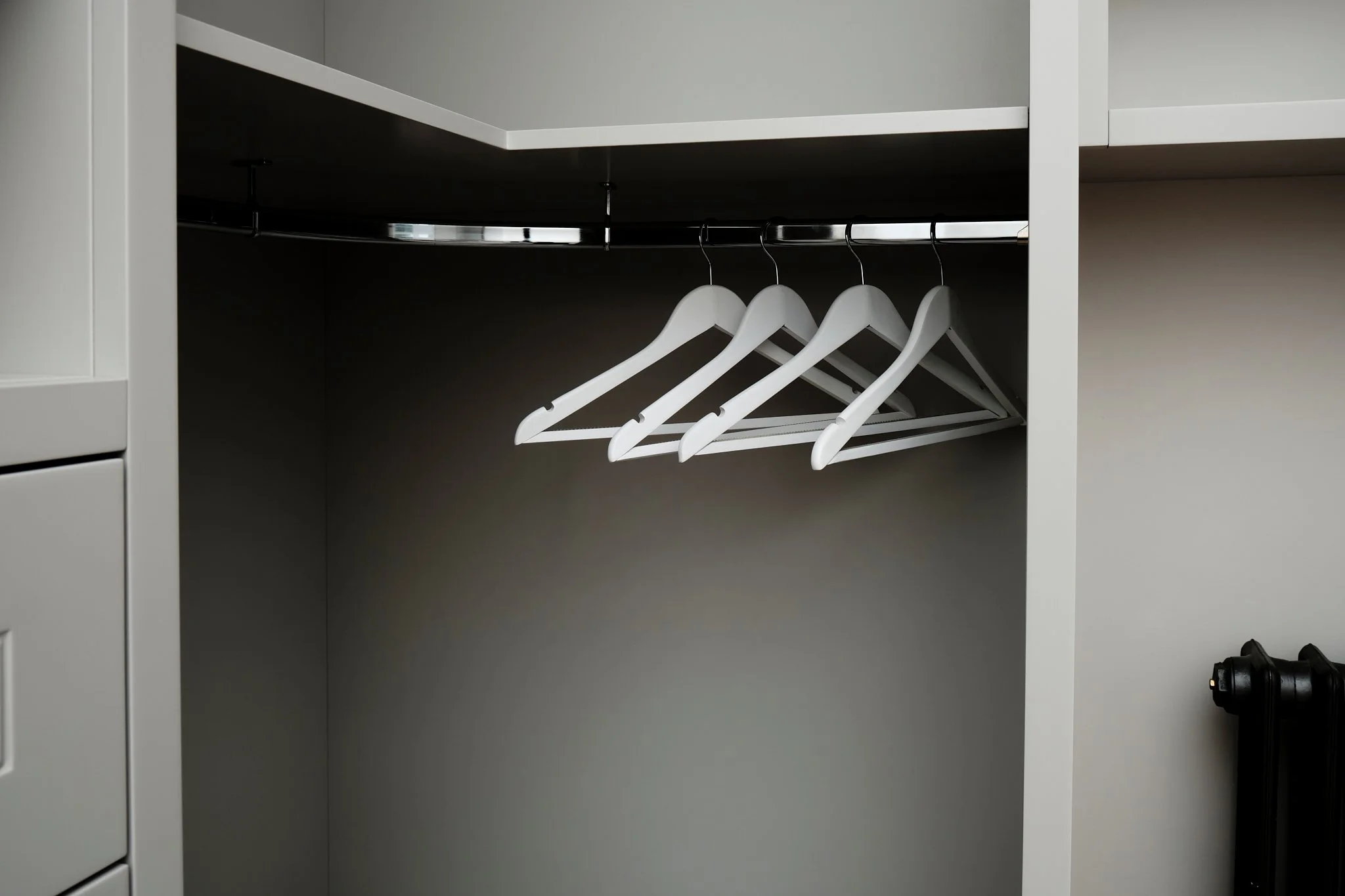 Empty closet with four white hangers hanging on a metal rod in a modern, gray-colored room.