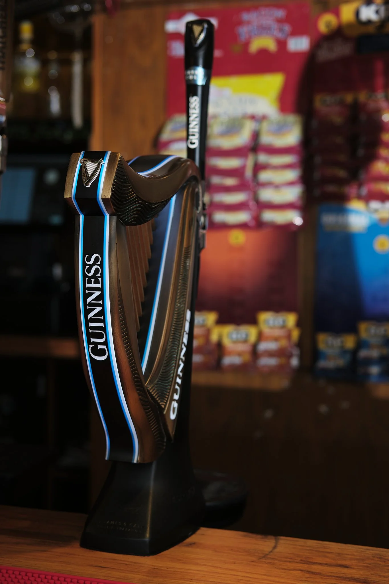 A Guinness-themed golf putter with a black grip, displayed on a wooden surface with snack bags and packaging in the blurred background.