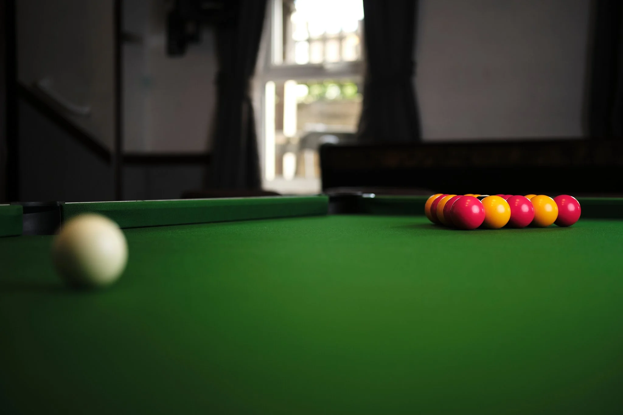 A green pool table with a set of collide balls arranged in a triangle and a white cue ball in the foreground.