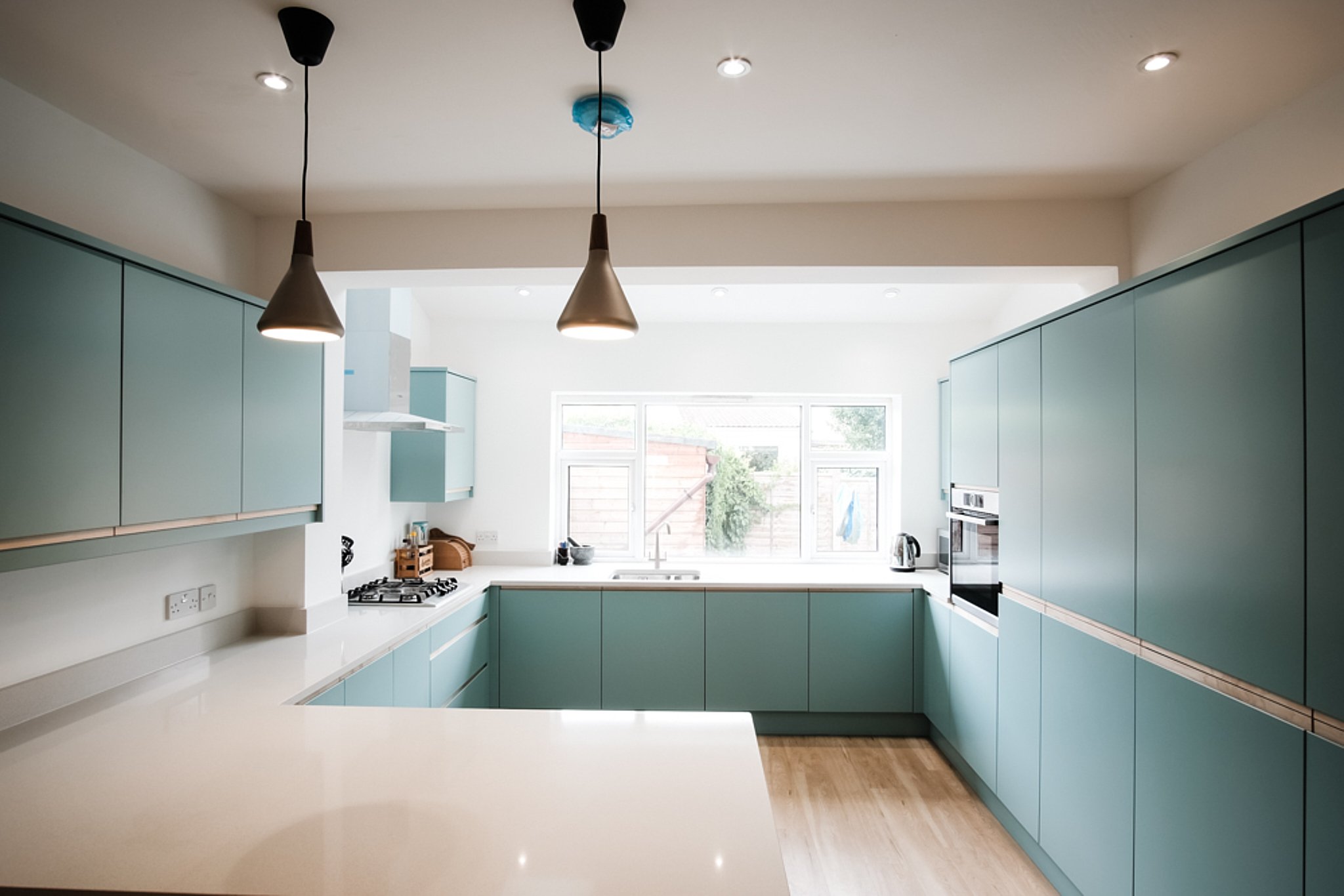 Modern kitchen with light blue cabinets, white countertops, large window, and minimal decor.