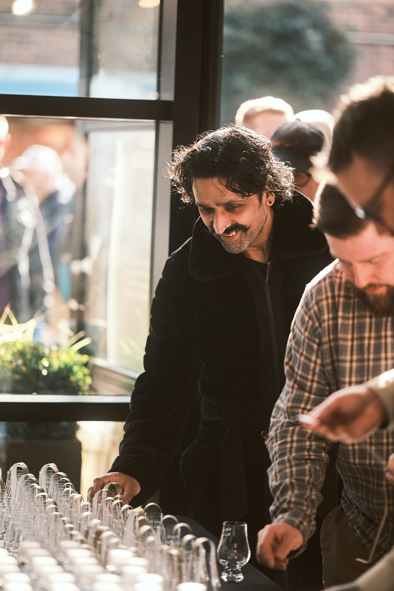 Man with curly dark hair and a mustache smiling while looking at a table of empty glasses.